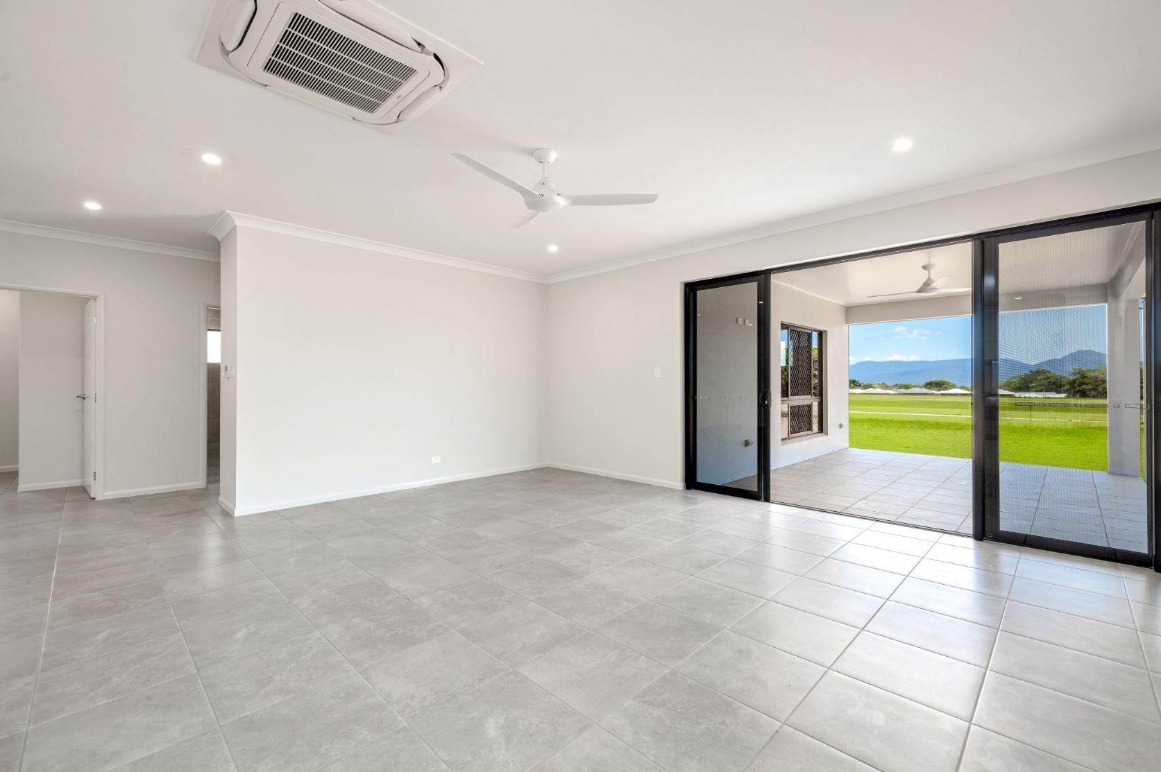 An Empty Living Room With Sliding Glass Doors and a Ceiling Fan — Ashlee Jones Homes in Gordonvale, QLD