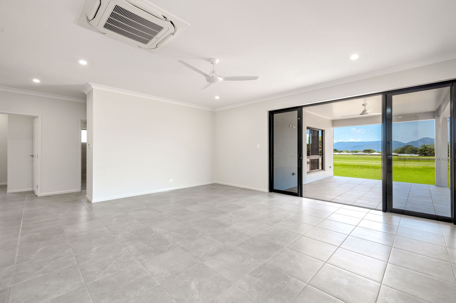 An Empty Living Room With Sliding Glass Doors and a Ceiling Fan — Ashlee Jones Homes in Gordonvale, QLD