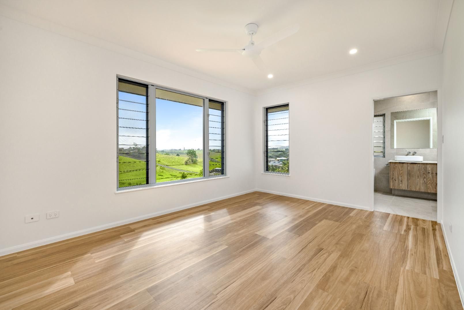 An Empty Room With Hardwood Floors and Two Windows — Ashlee Jones Homes in Gordonvale, QLD