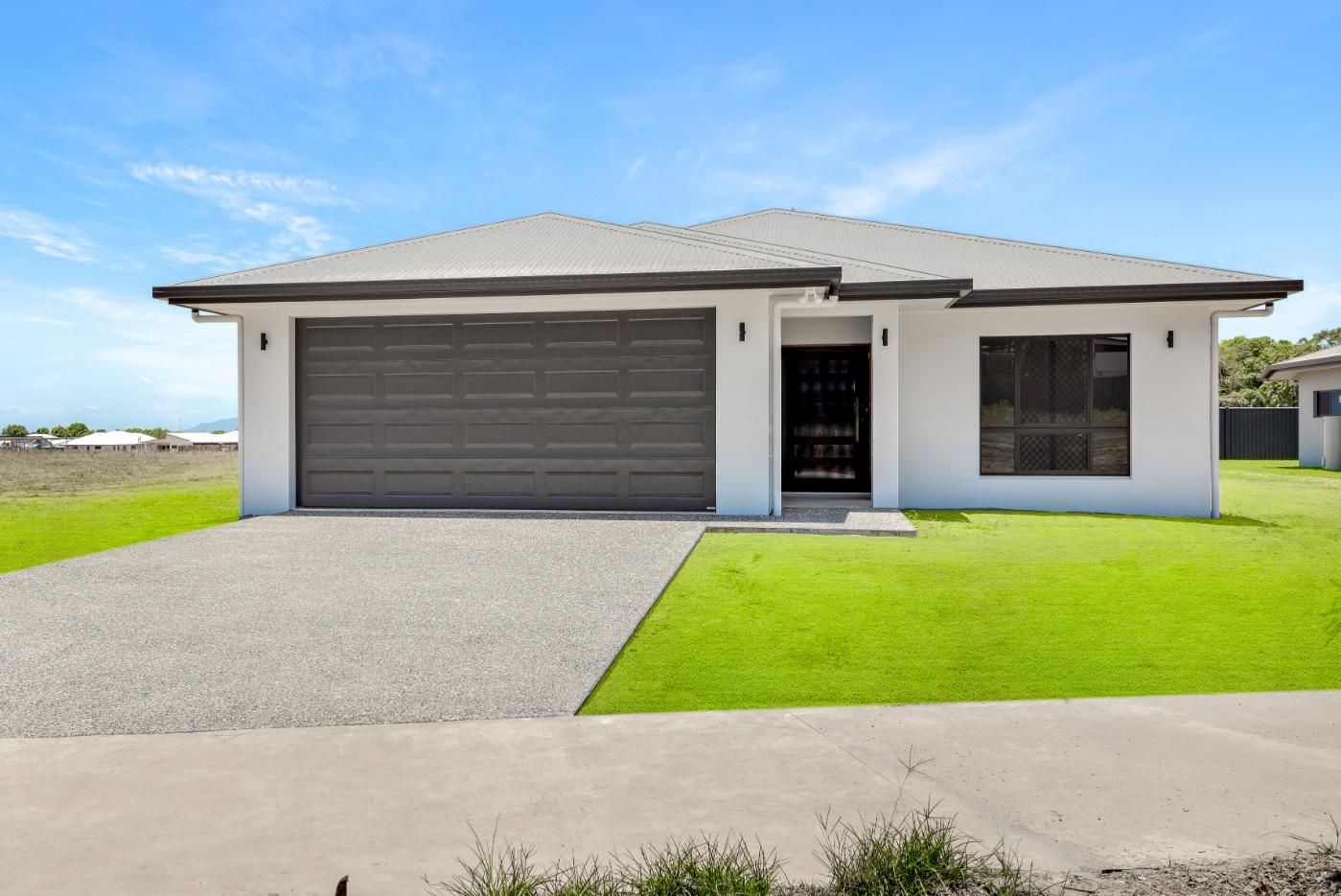 A White House With a Gray Garage Door and a Concrete Driveway — Ashlee Jones Homes in Gordonvale, QLD