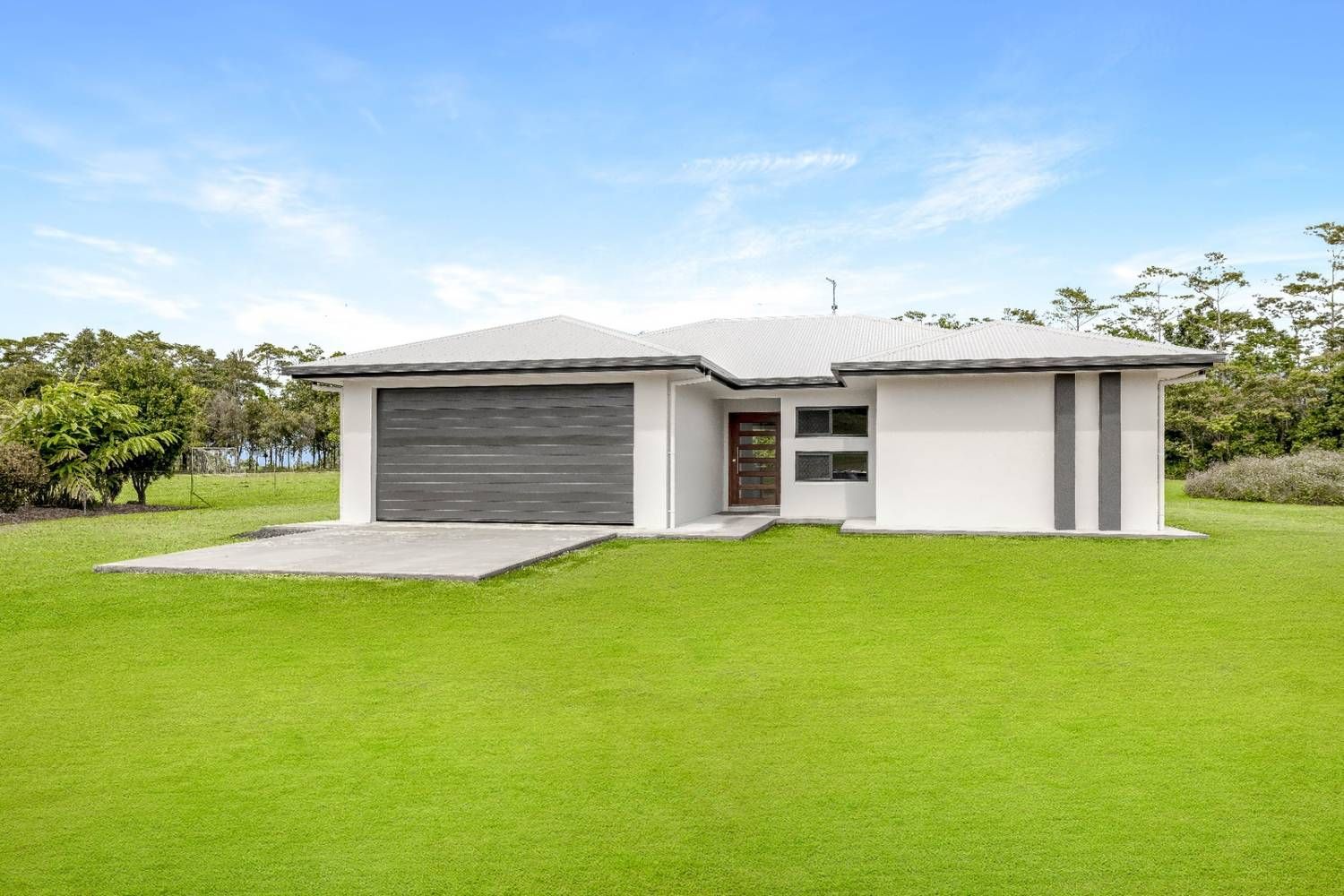 A White House With a Gray Garage Door is Sitting on Top of a Lush Green Field — Ashlee Jones Homes in Gordonvale, QLD