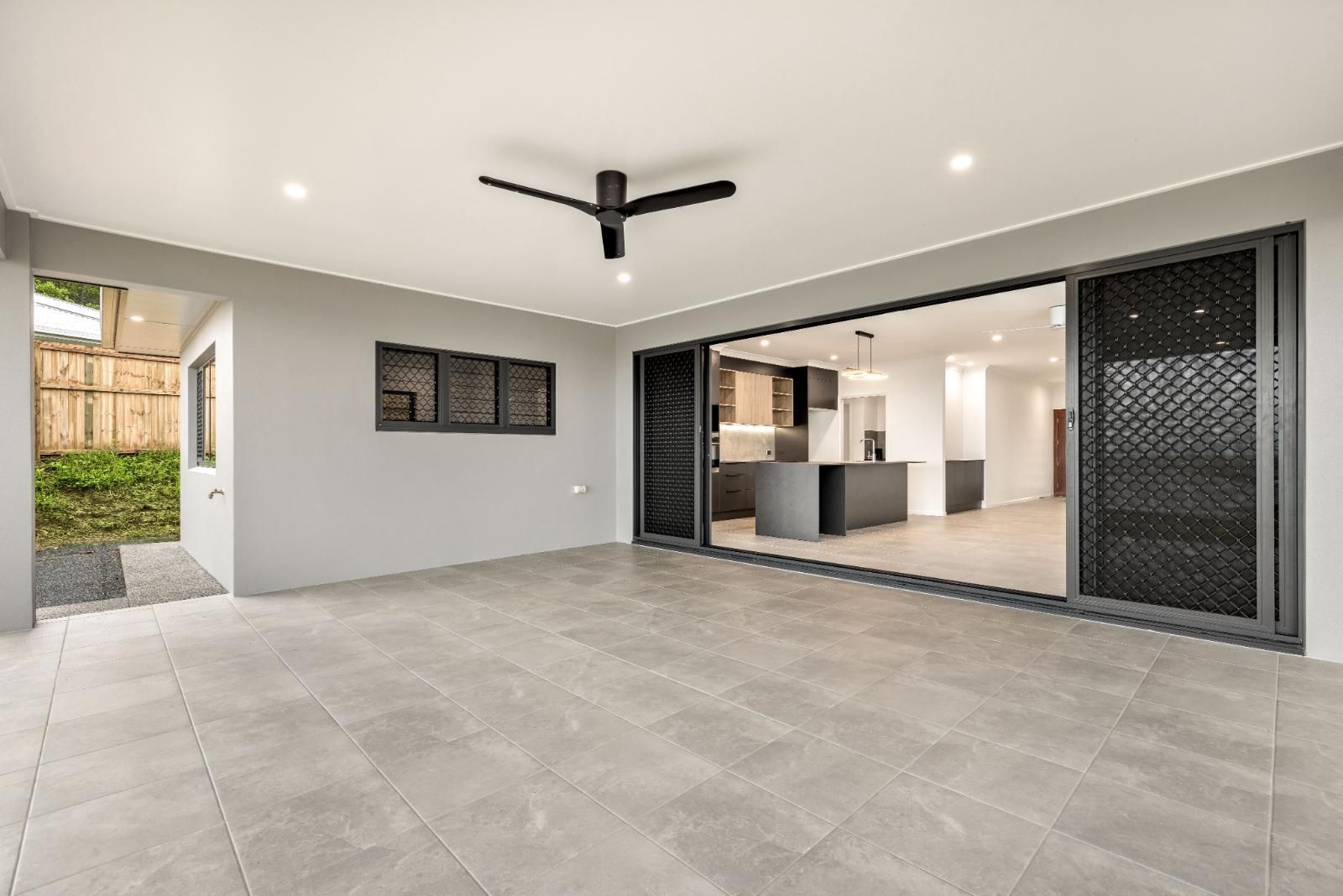 An Empty Room With a Ceiling Fan and Sliding Glass Doors Leading to a Kitchen — Ashlee Jones Homes in Gordonvale, QLD