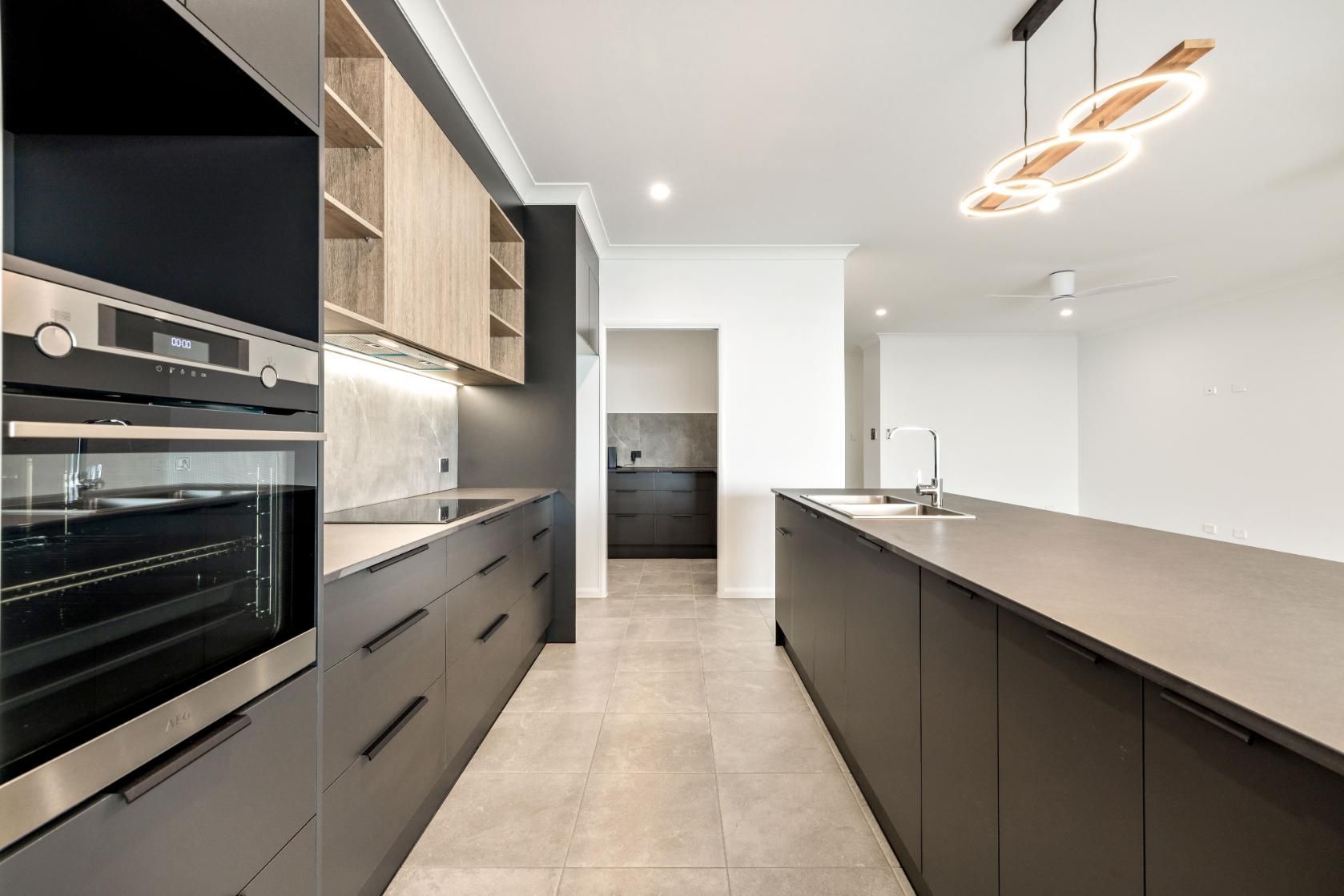 A Kitchen With Black Cabinets, Stainless Steel Appliances, and a Large Island — Ashlee Jones Homes in Gordonvale, QLD