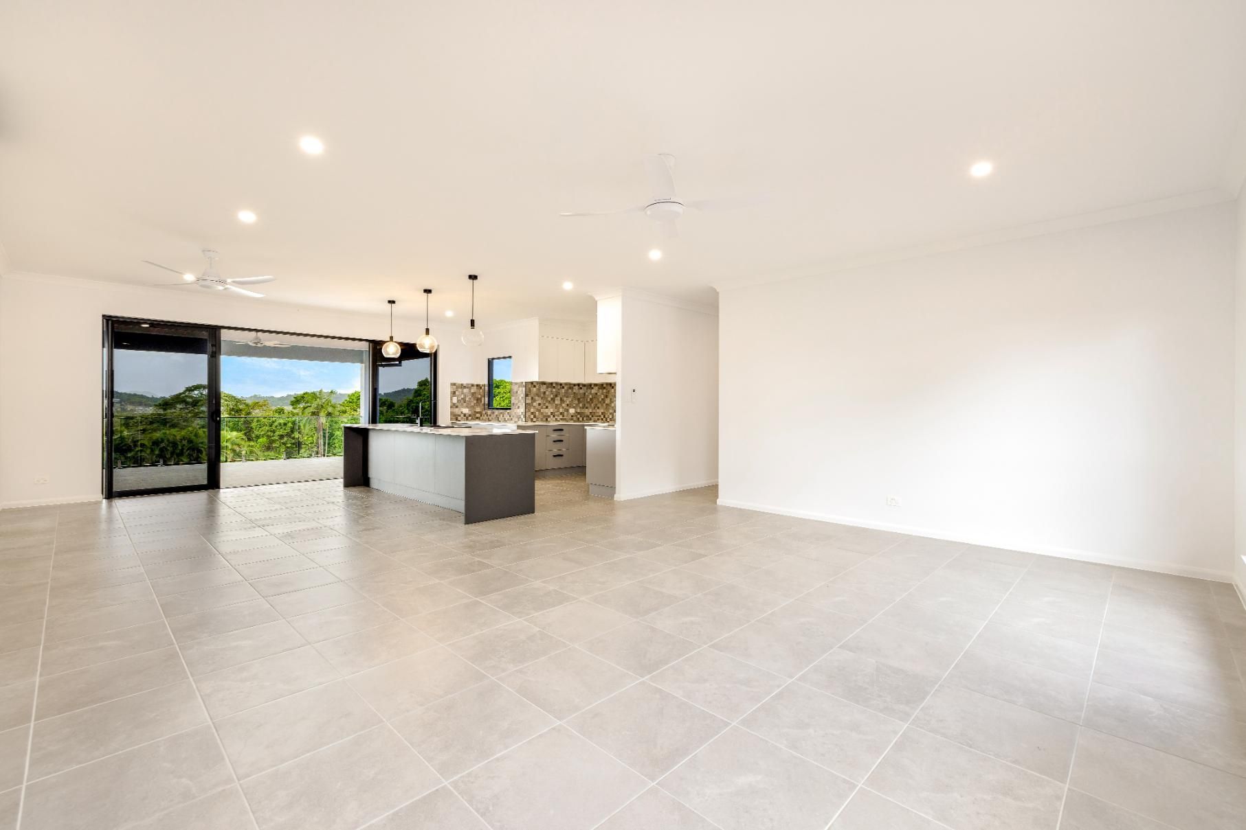 A Large Empty Room With a Tiled Floor and a Kitchen in the Background — Ashlee Jones Homes in Gordonvale, QLD
