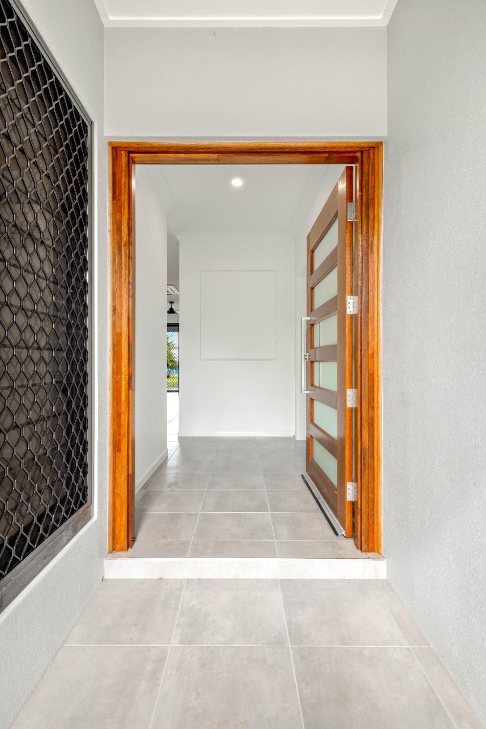A Hallway With a Wooden Door and a Tiled Floor — Ashlee Jones Homes in Gordonvale, QLD