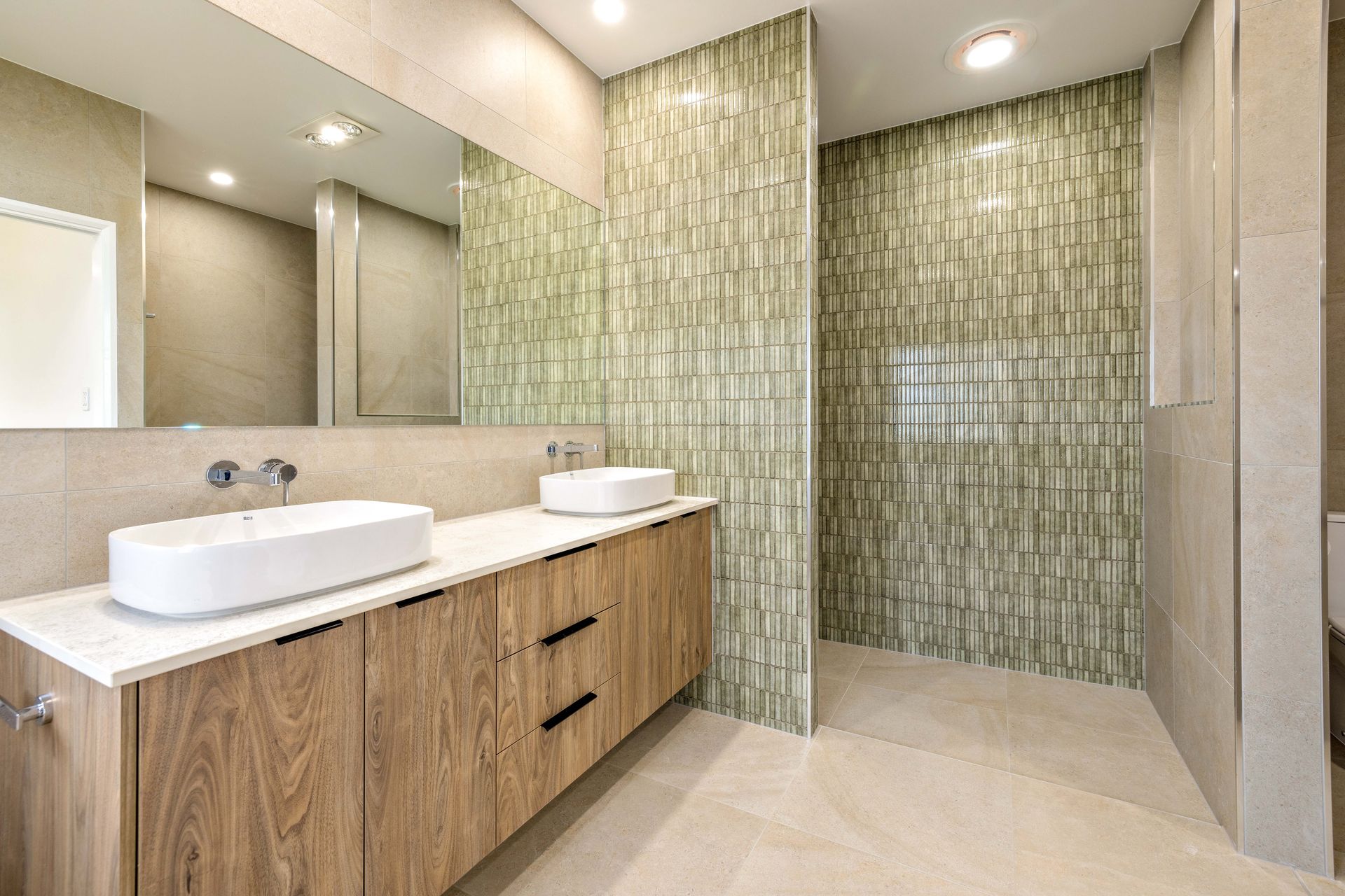Modern bathroom with wooden vanity, two sinks, green tiled shower, and large mirror. — Ashlee Jones Homes in Gordonvale, QLD