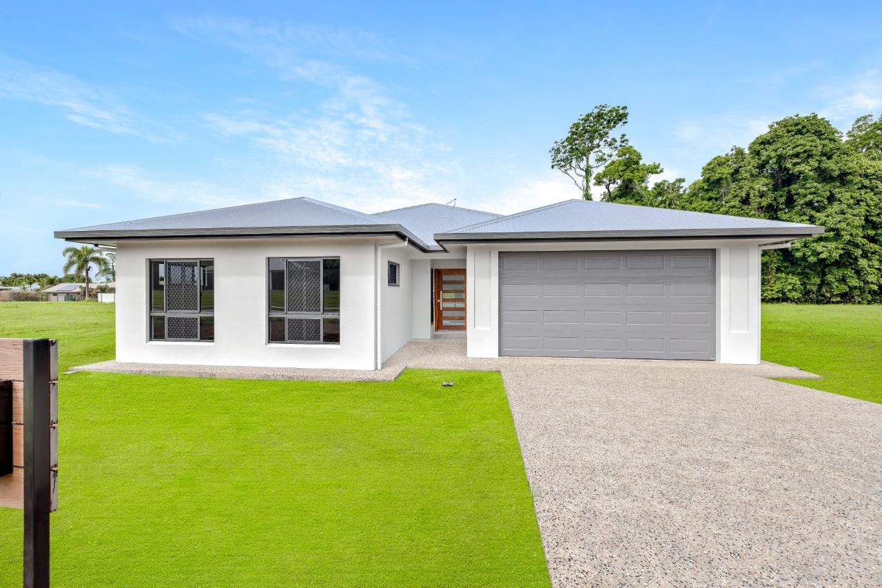 A White House With a Gray Garage Door is Sitting on Top of a Lush Green Field — Ashlee Jones Homes in Gordonvale, QLD