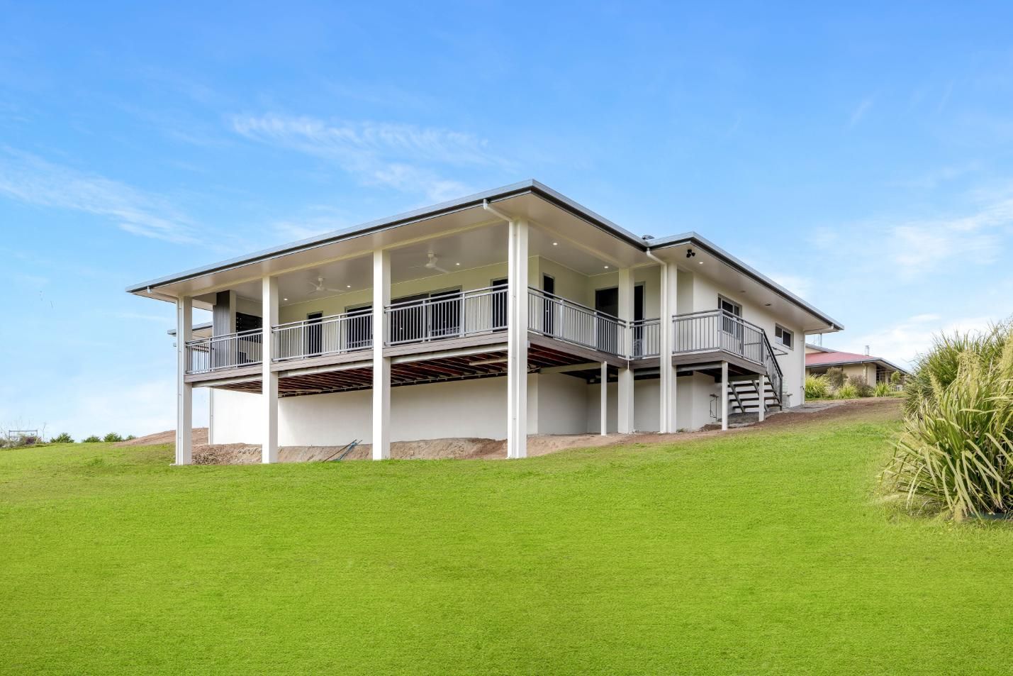 A Large White House is Sitting on Top of a Lush Green Hill — Ashlee Jones Homes in Gordonvale, QLD