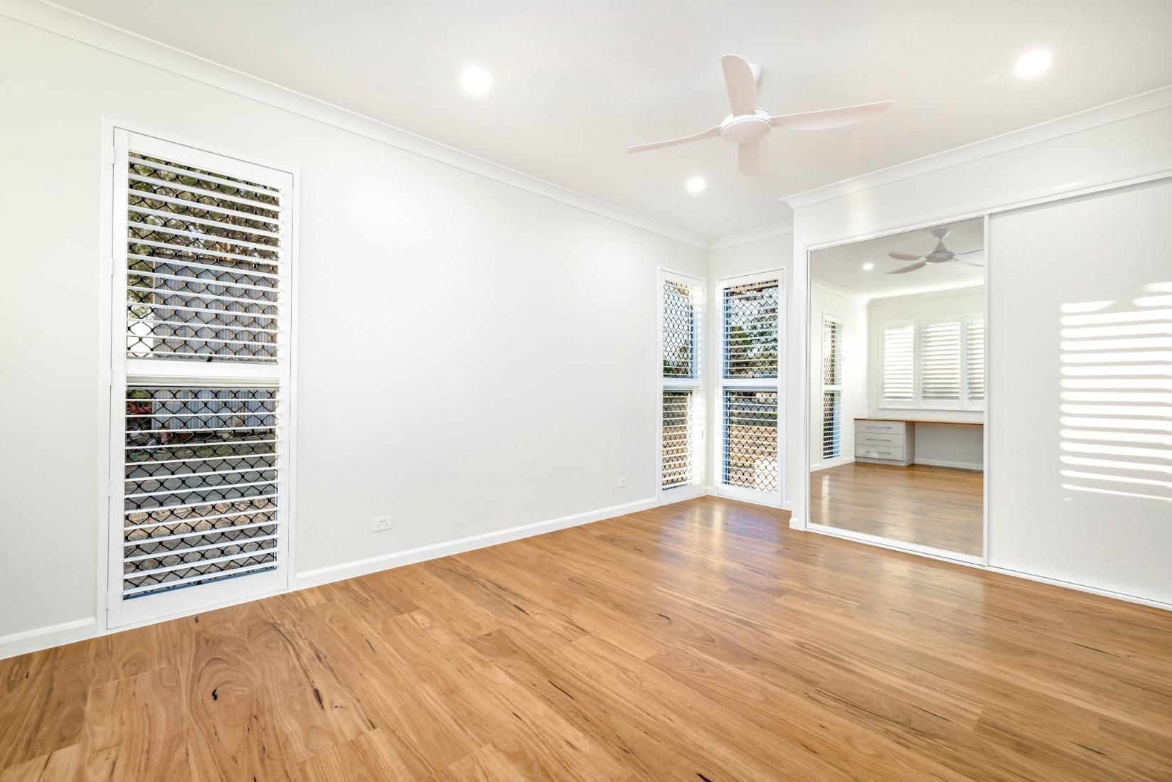 An Empty Room With Hardwood Floors, White Walls and a Ceiling Fan — Ashlee Jones Homes in Gordonvale, QLD