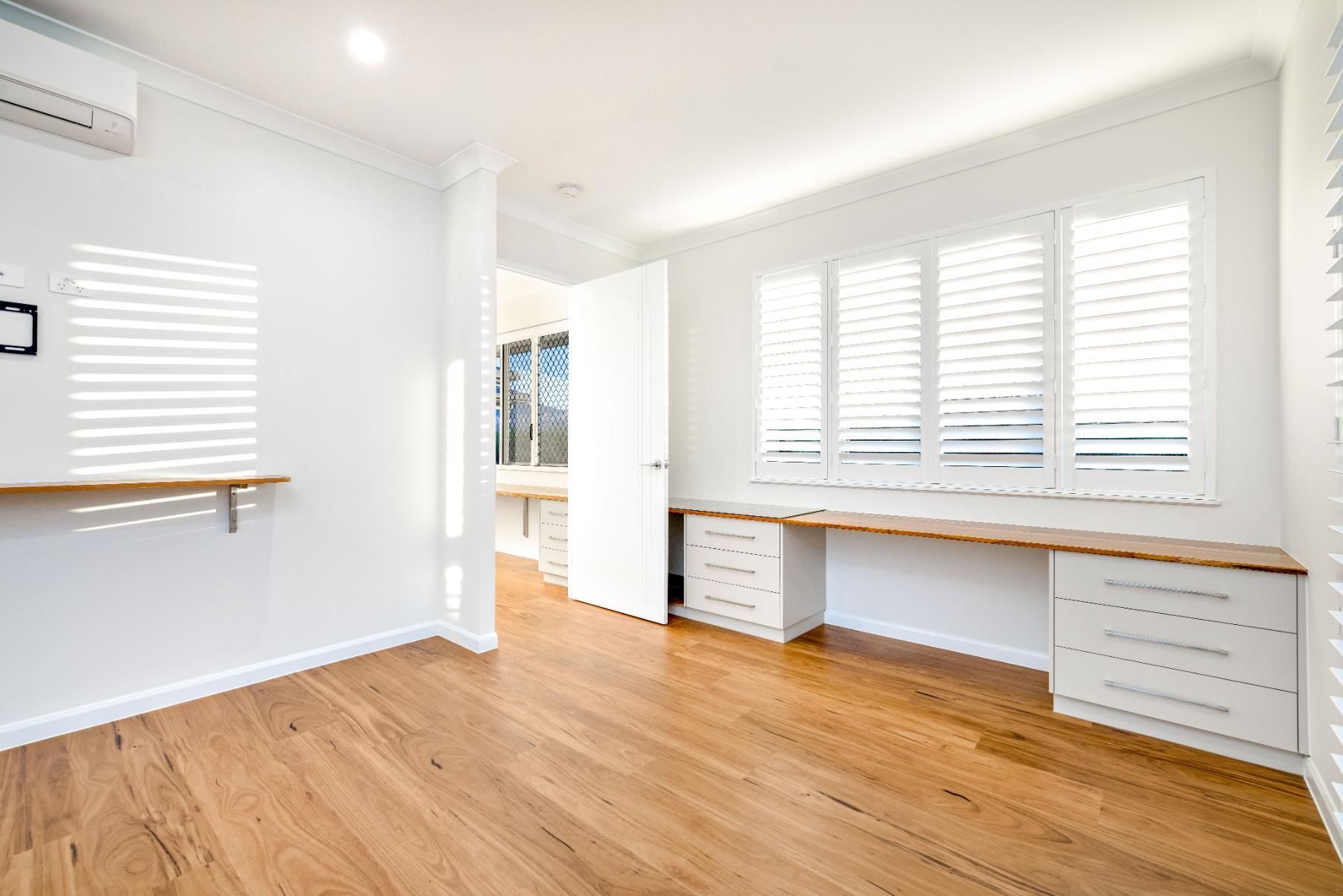 An Empty Room With Hardwood Floors, White Walls and Shutters — Ashlee Jones Homes in Gordonvale, QLD