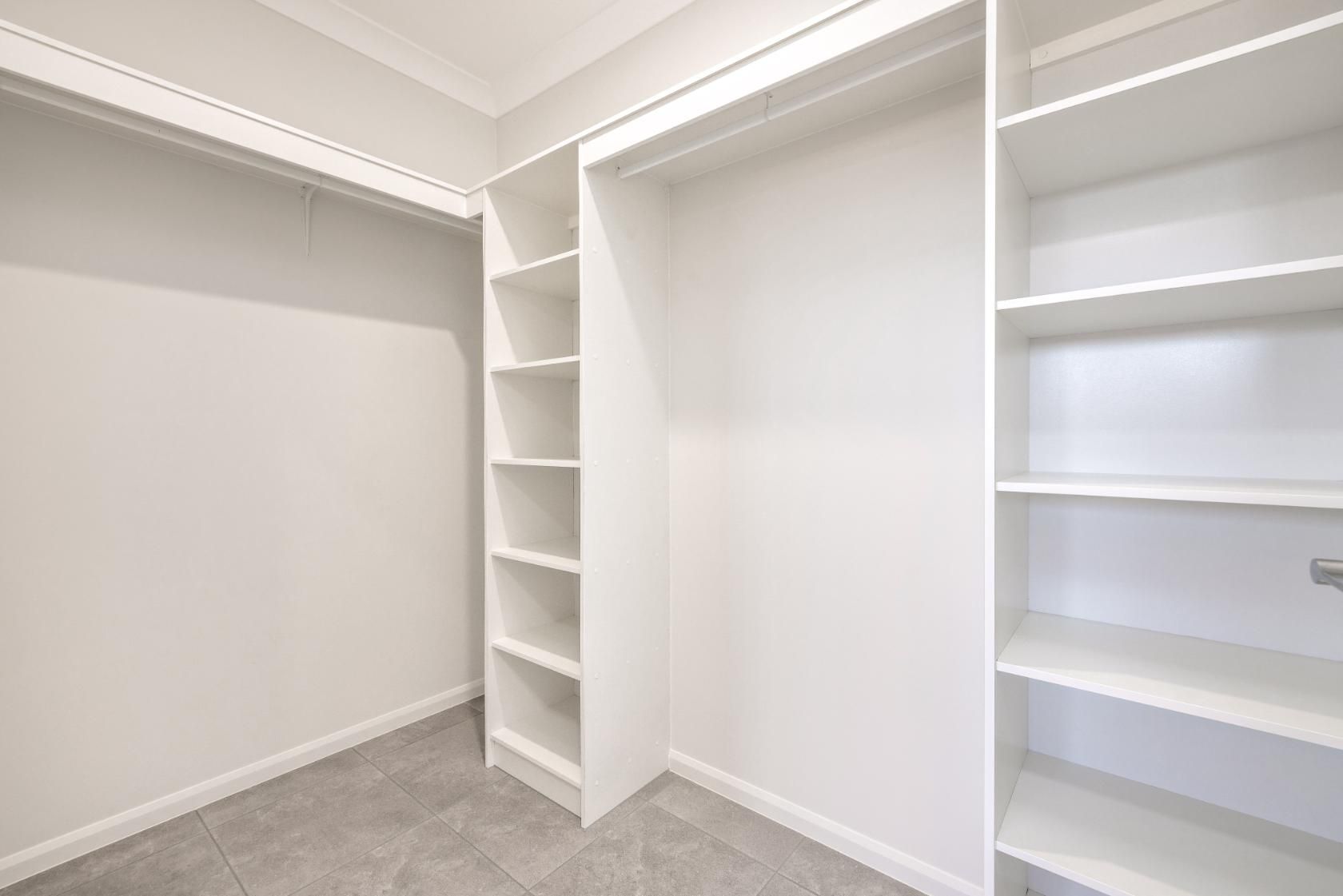 An Empty Walk in Closet With White Shelves and a Gray Carpet — Ashlee Jones Homes in Gordonvale, QLD