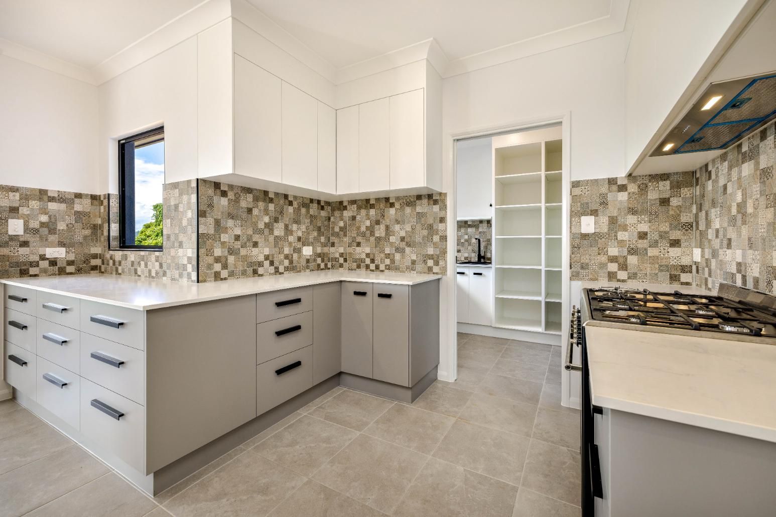 An Empty Kitchen With White Cabinets, a Stove, and a Window — Ashlee Jones Homes in Gordonvale, QLD
