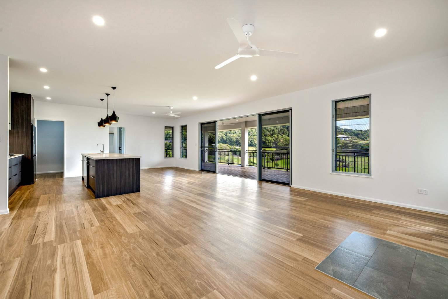 A Large Empty Room With Hardwood Floors and a Ceiling Fan — Ashlee Jones Homes in Gordonvale, QLD