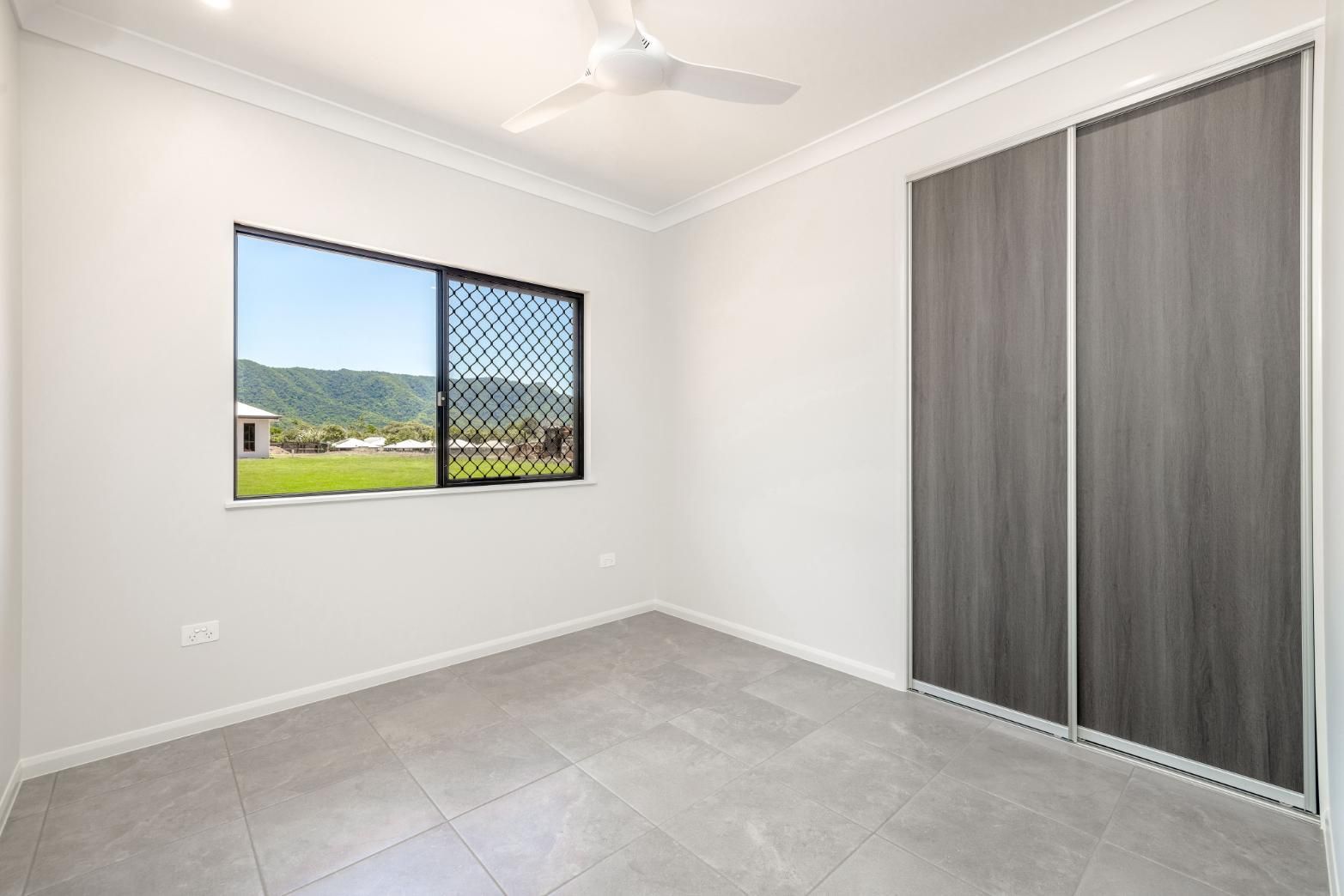 An Empty Bedroom With a Window and a Ceiling Fan — Ashlee Jones Homes in Gordonvale, QLD