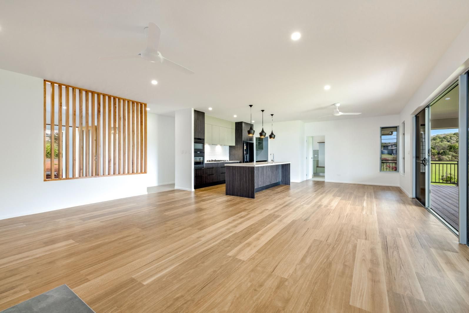 A Large Empty Room With Hardwood Floors and a Kitchen — Ashlee Jones Homes in Gordonvale, QLD