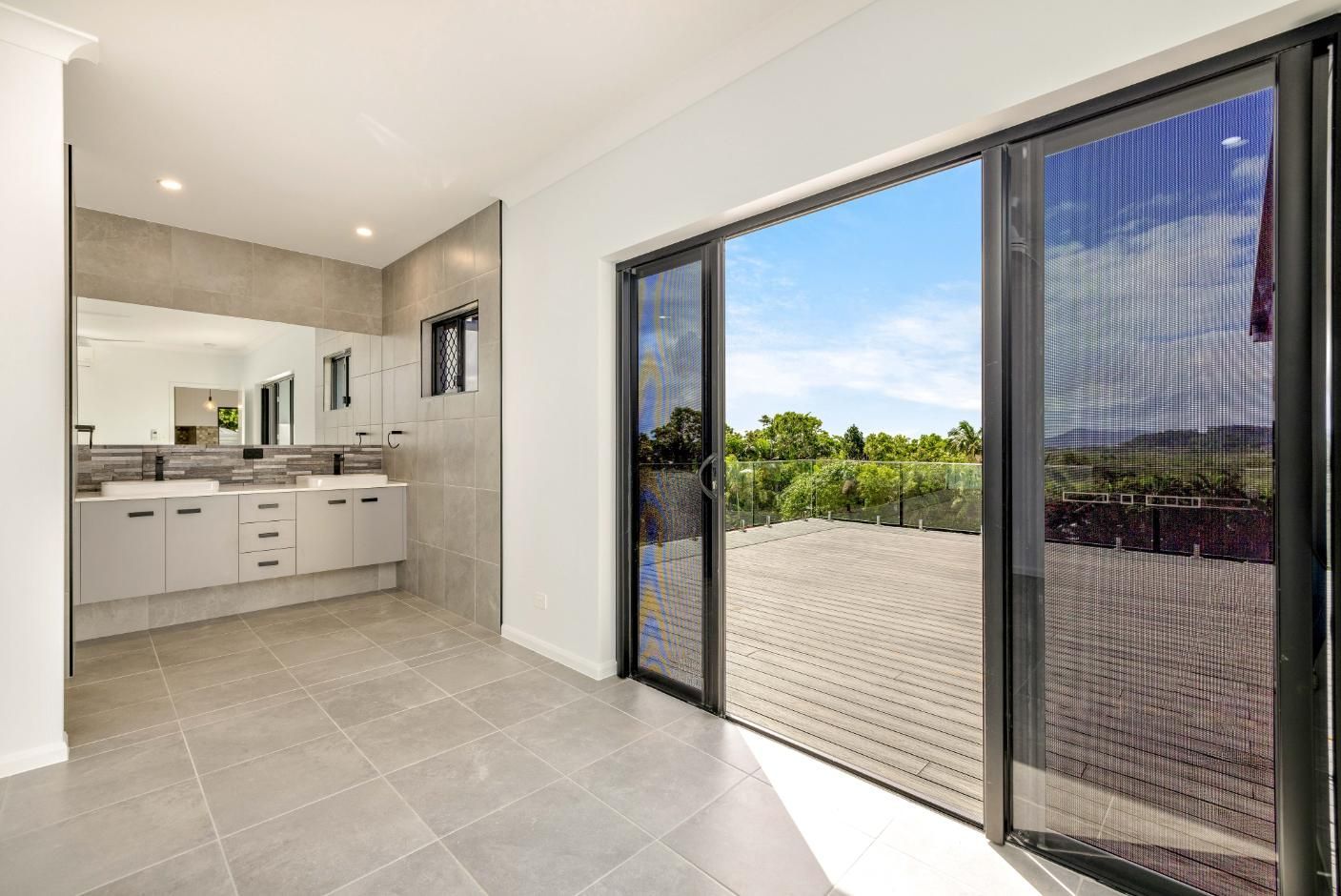 A Bathroom With Two Sinks and a Sliding Glass Door Leading to a Deck — Ashlee Jones Homes in Gordonvale, QLD