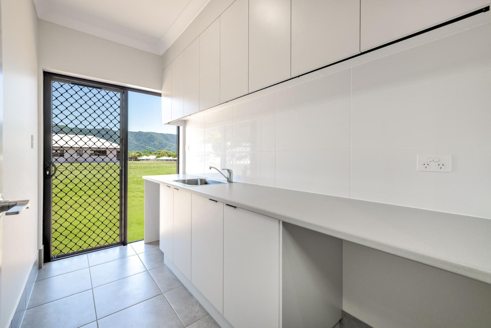 A Kitchen With White Cabinets, a Sink, and a Sliding Glass Door — Ashlee Jones Homes in Gordonvale, QLD