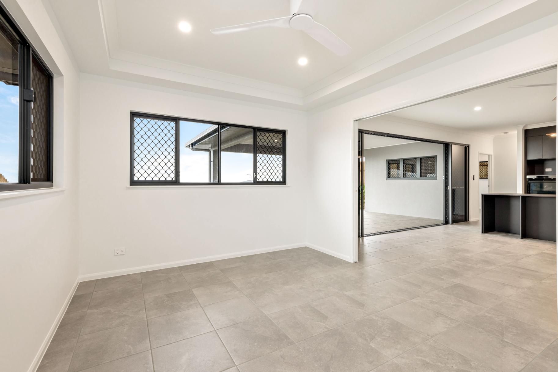 An Empty Living Room With a Ceiling Fan and Two Windows — Ashlee Jones Homes in Gordonvale, QLD