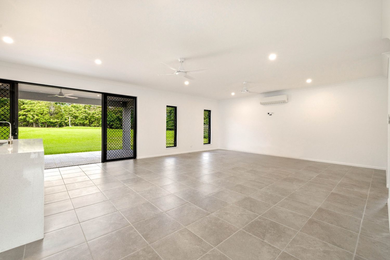 A Large Empty Room With a Tiled Floor and Sliding Glass Doors — Ashlee Jones Homes in Gordonvale, QLD