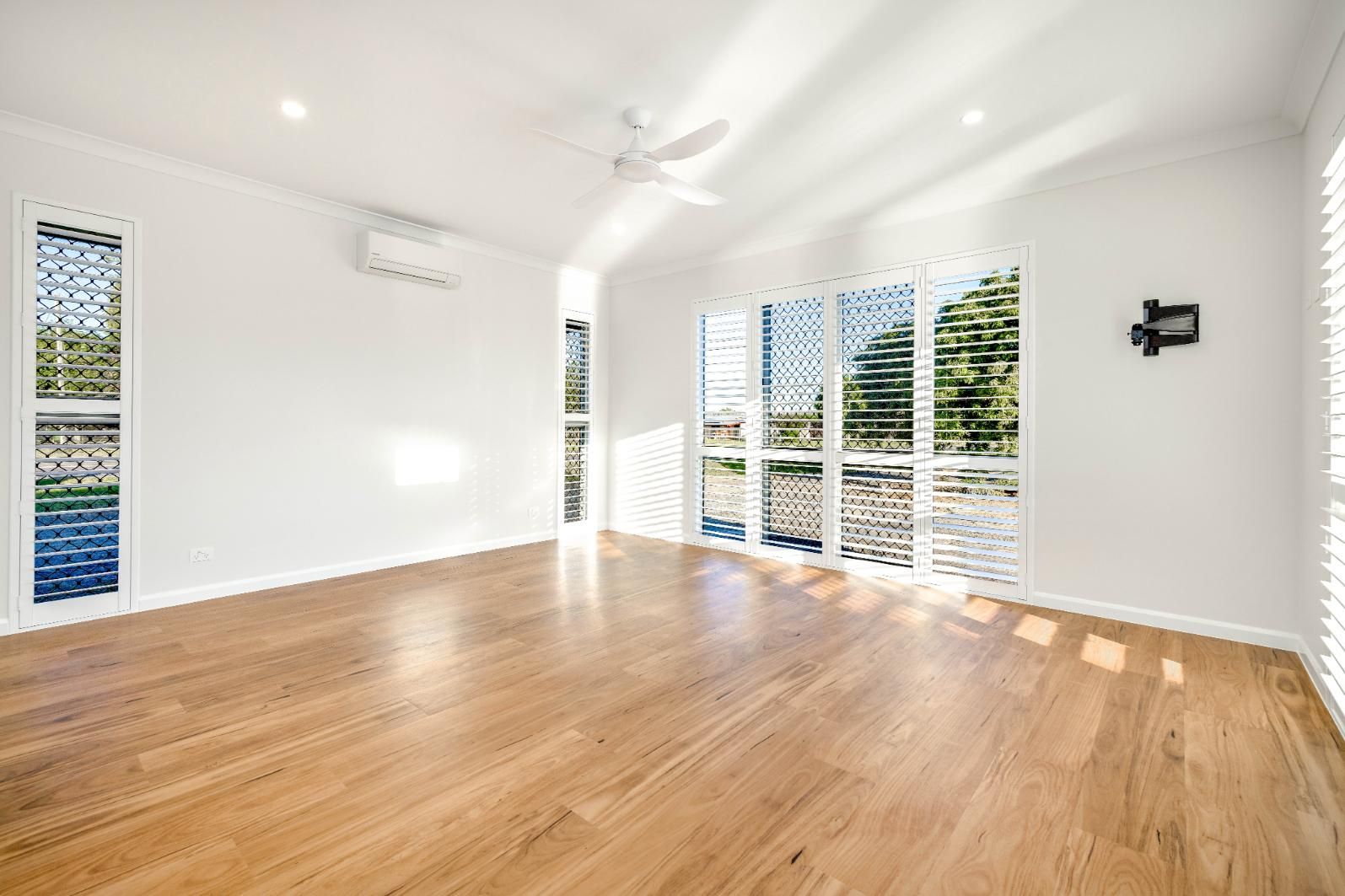An Empty Living Room With Hardwood Floors, White Walls and Sliding Glass Doors — Ashlee Jones Homes in Gordonvale, QLD