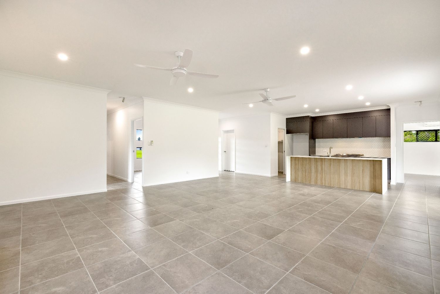 A Large Empty Room With a Tiled Floor and a Kitchen in the Background — Ashlee Jones Homes in Gordonvale, QLD