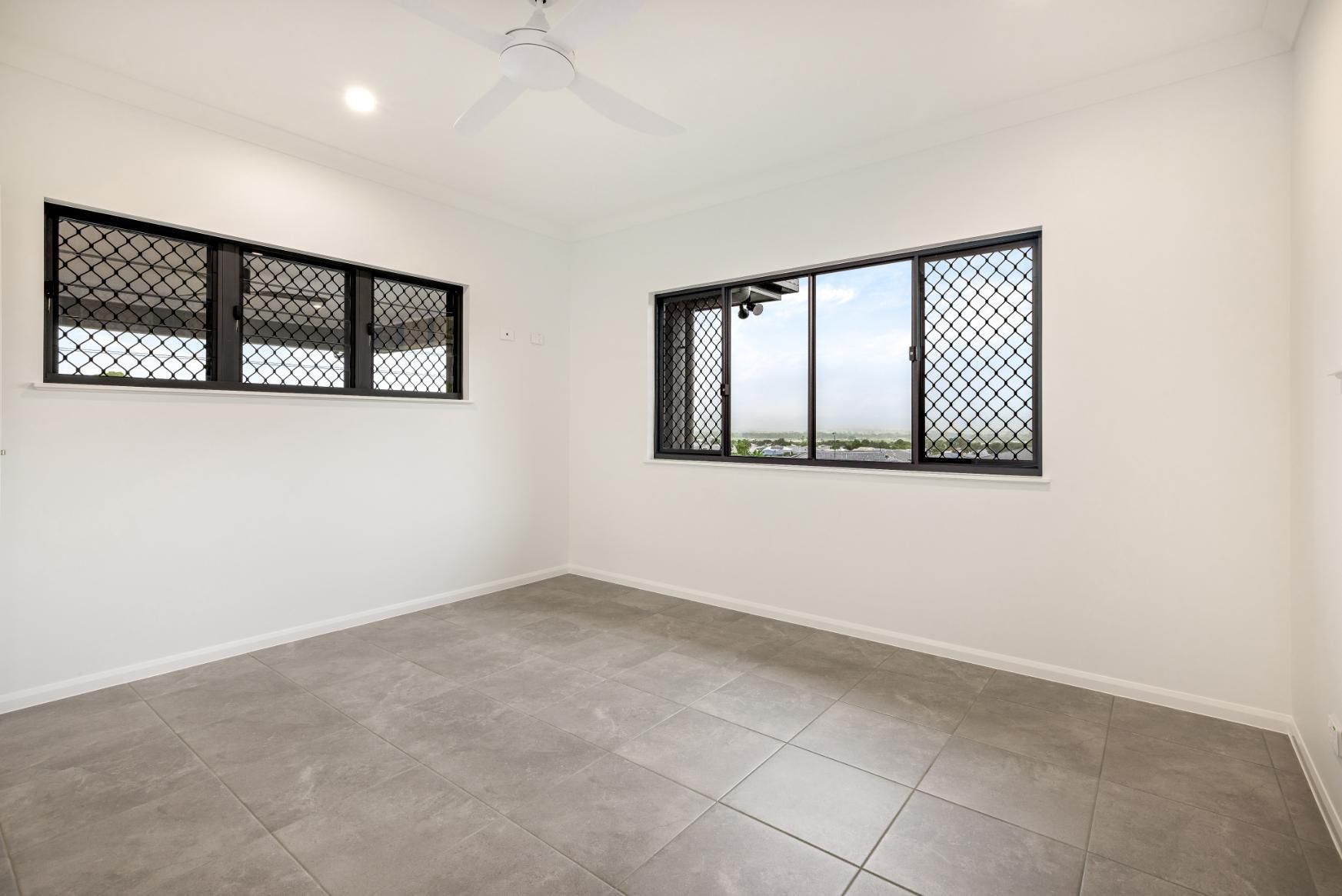 An Empty Room With Two Windows and a Ceiling Fan — Ashlee Jones Homes in Gordonvale, QLD