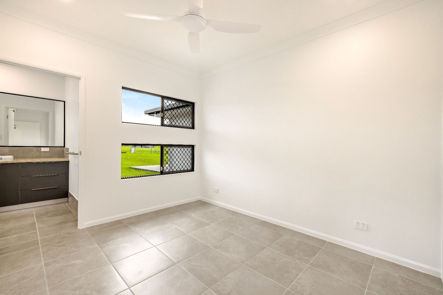An Empty Bedroom With a Ceiling Fan and Two Windows — Ashlee Jones Homes in Gordonvale, QLD