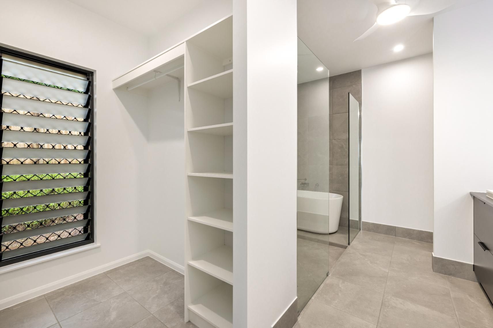 A Walk in Closet Next to a Bathroom With a Bathtub — Ashlee Jones Homes in Gordonvale, QLD