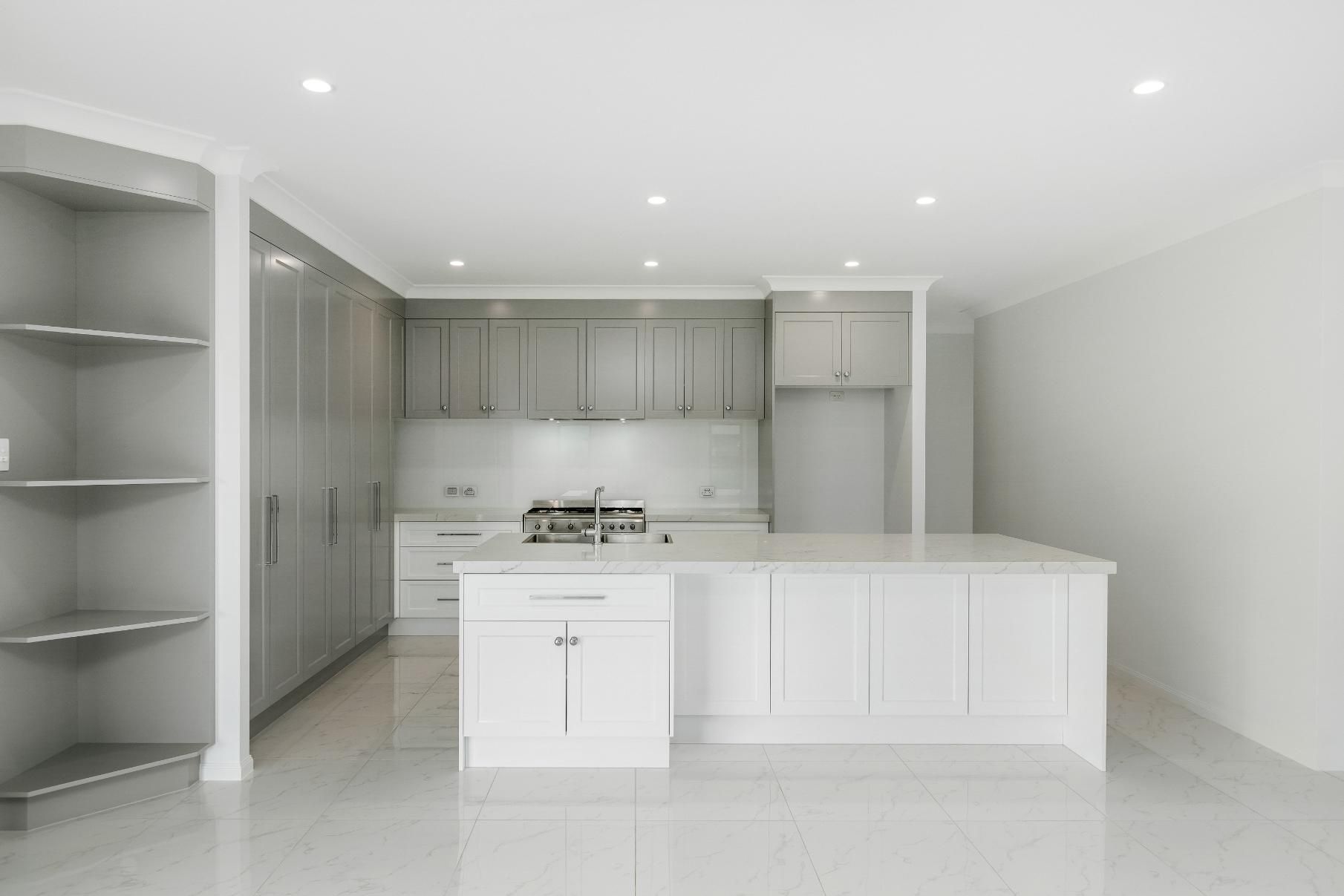 An Empty Kitchen With White Cabinets and a Large Island — Ashlee Jones Homes in Gordonvale, QLD