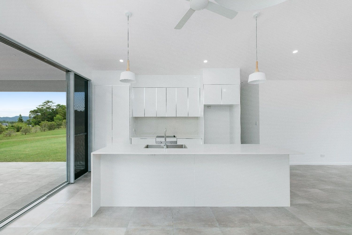 An Empty Kitchen With White Cabinets and a Ceiling Fan — Ashlee Jones Homes in Gordonvale, QLD