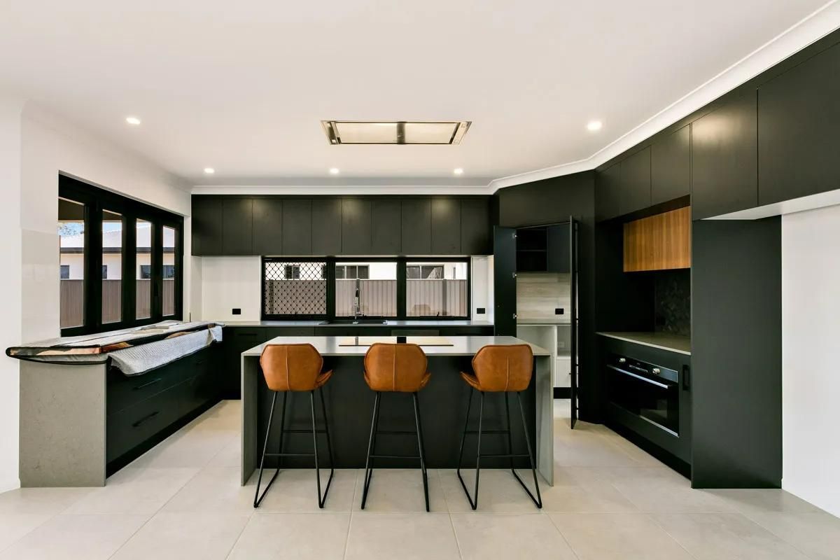 A Kitchen With Black Cabinets and Stools and a Large Island — Ashlee Jones Homes in Gordonvale, QLD