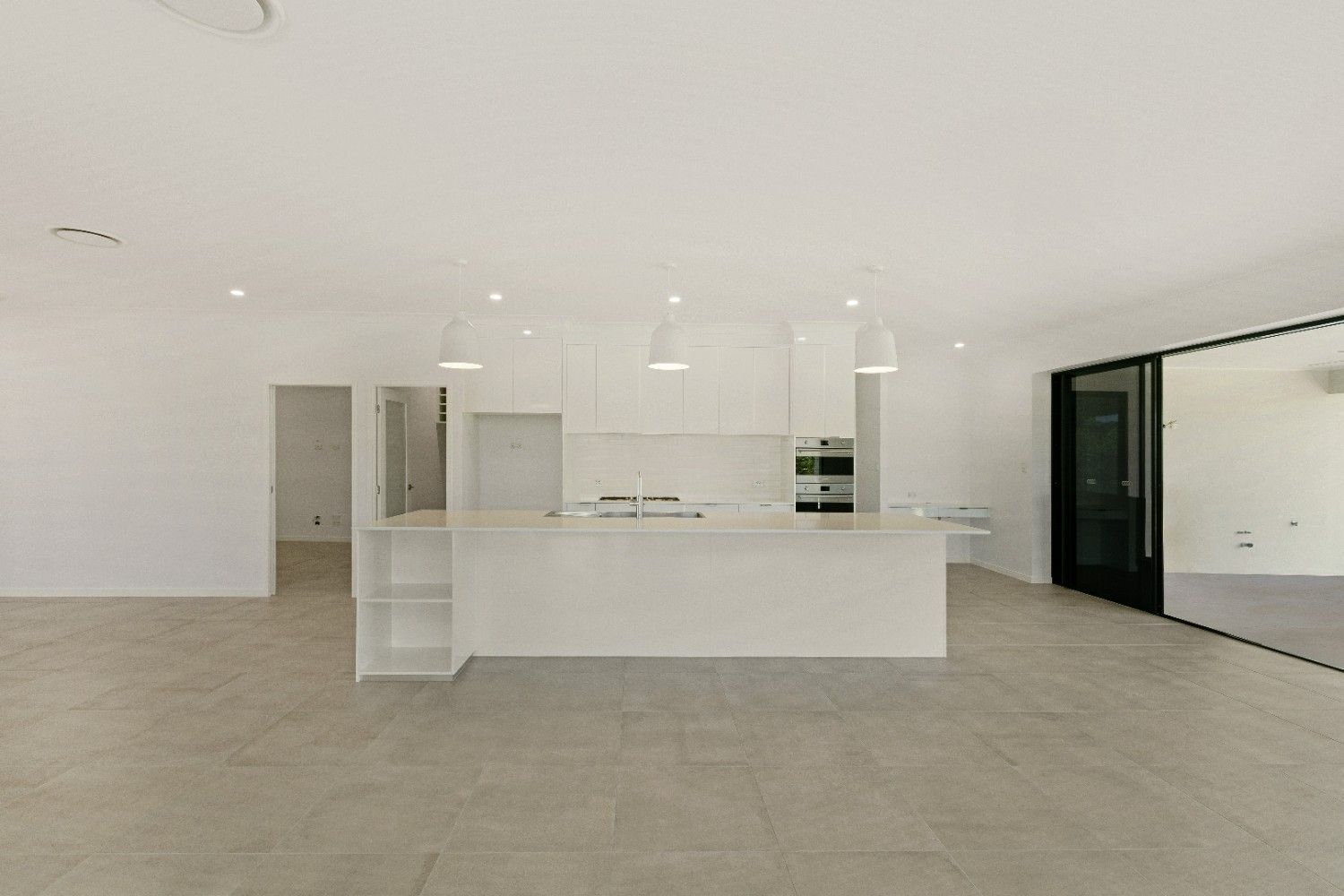 An Empty Kitchen With White Cabinets and a Large Island — Ashlee Jones Homes in Gordonvale, QLD