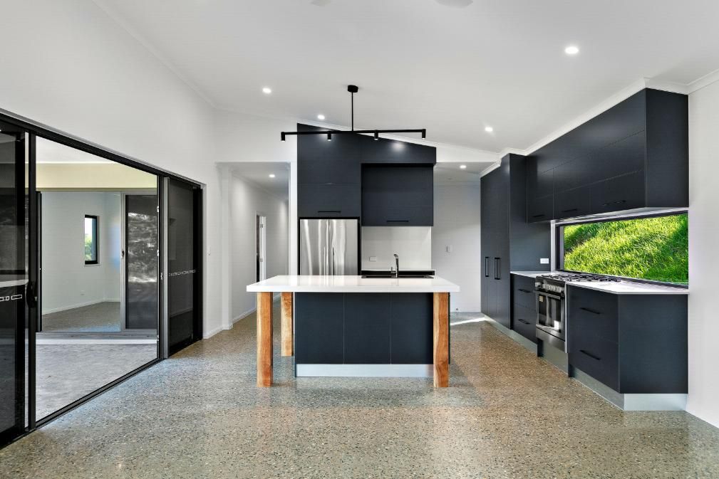 A Kitchen With Black Cabinets and a Large Island in the Middle of the Room — Ashlee Jones Homes in Gordonvale, QLD