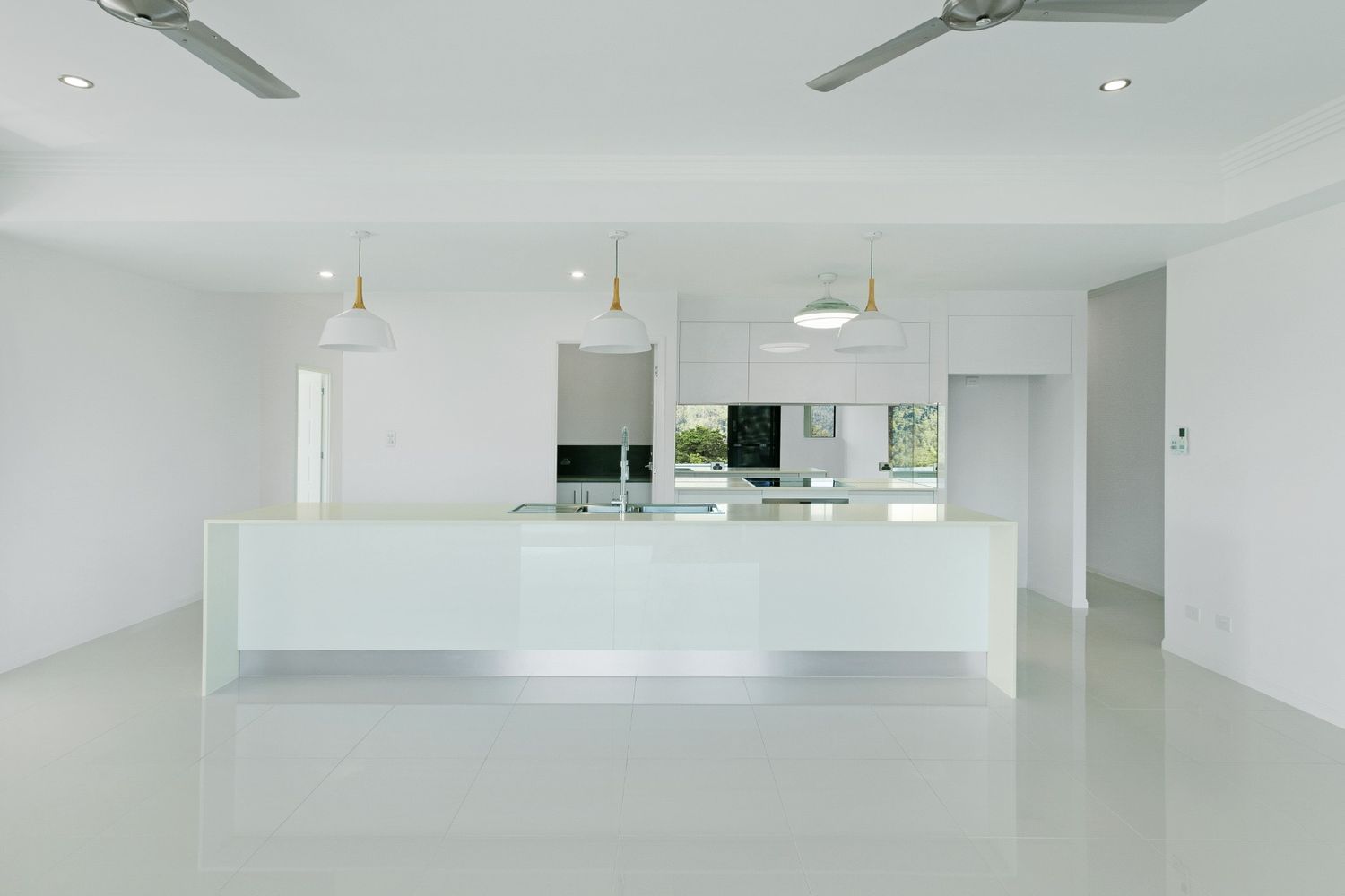 An Empty Kitchen With a Large Island and Two Ceiling Fans — Ashlee Jones Homes in Gordonvale, QLD