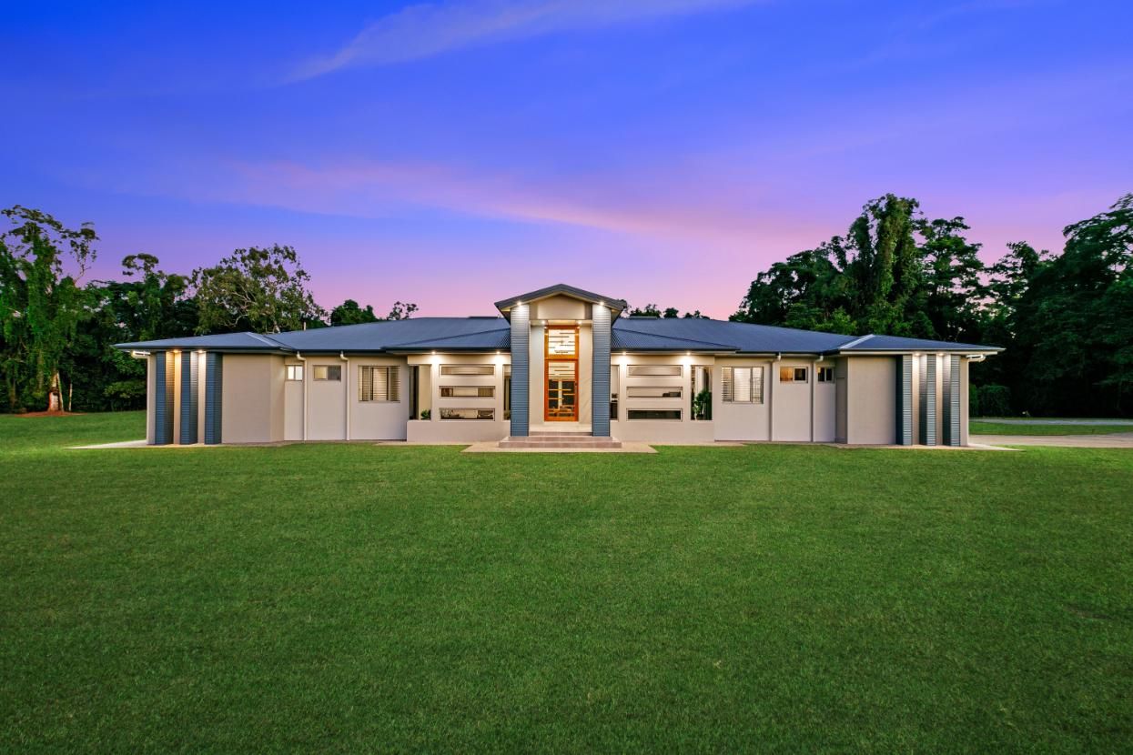 A Large House With a Brown Door  is Sitting on Top of a Lush Green Field — Ashlee Jones Homes in Gordonvale, QLD