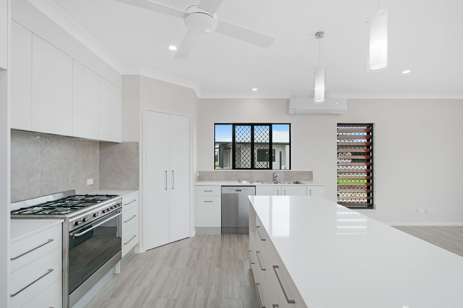 A Kitchen With White Cabinets , Stainless Steel Appliances , and a Large Island — Ashlee Jones Homes in Gordonvale, QLD