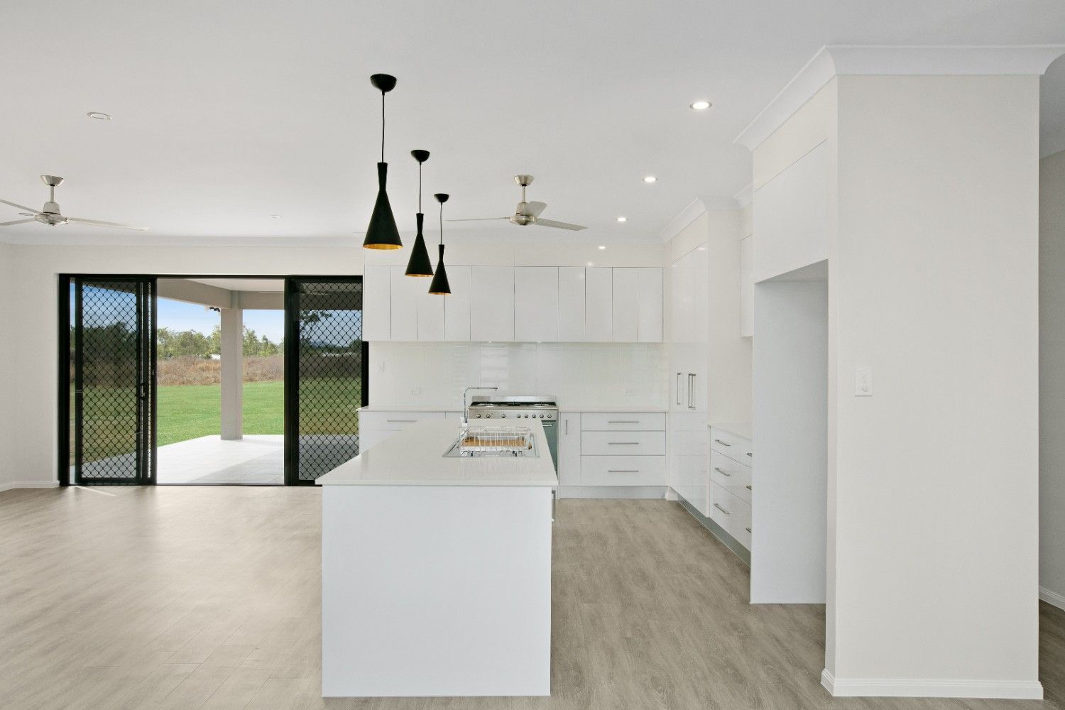 A Kitchen in an Empty House With White Cabinets and a Large Island — Ashlee Jones Homes in Gordonvale, QLD