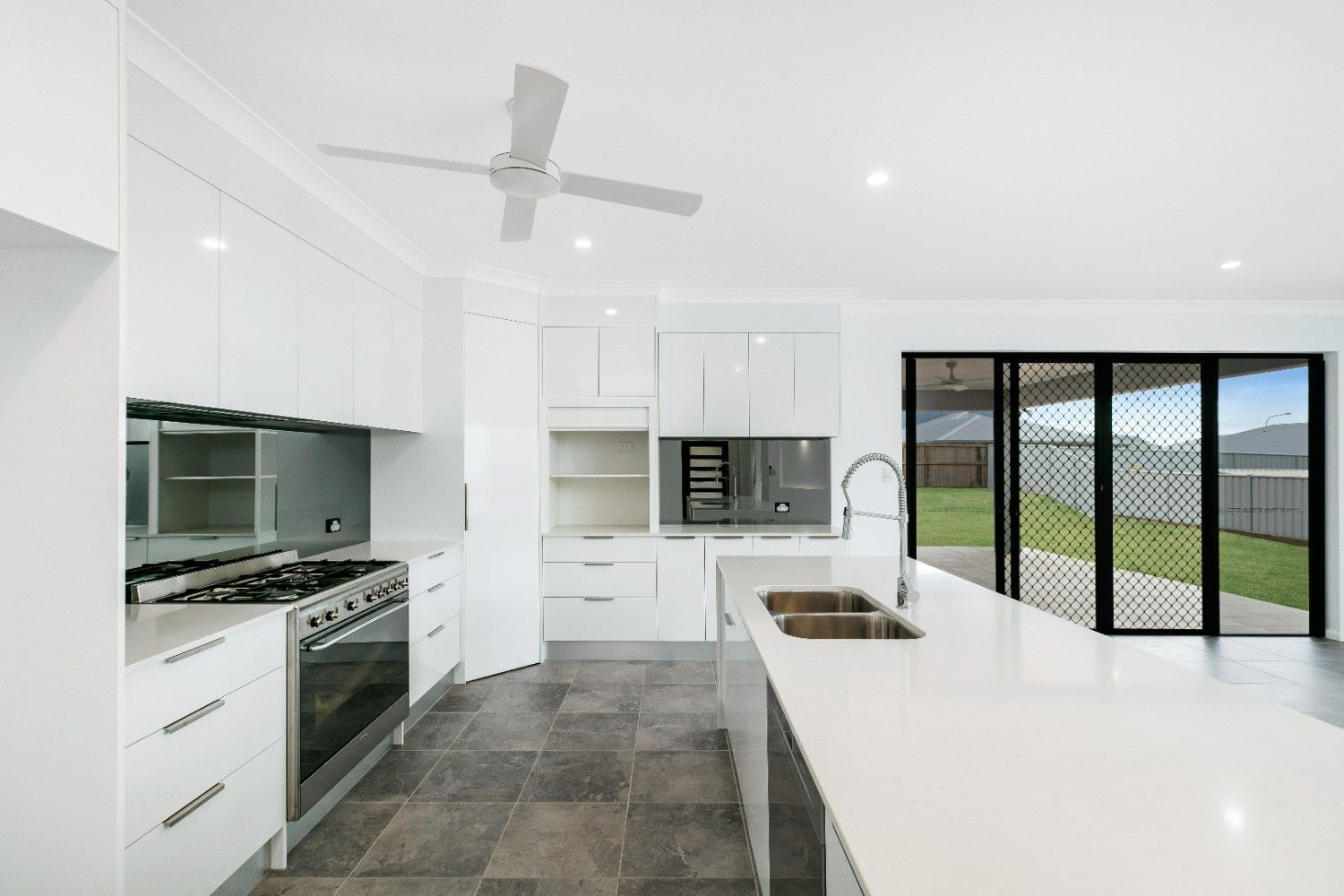 A Kitchen With White Cabinets, Stainless Steel Appliances, a Sink and a Ceiling Fan — Ashlee Jones Homes in Gordonvale, QLD