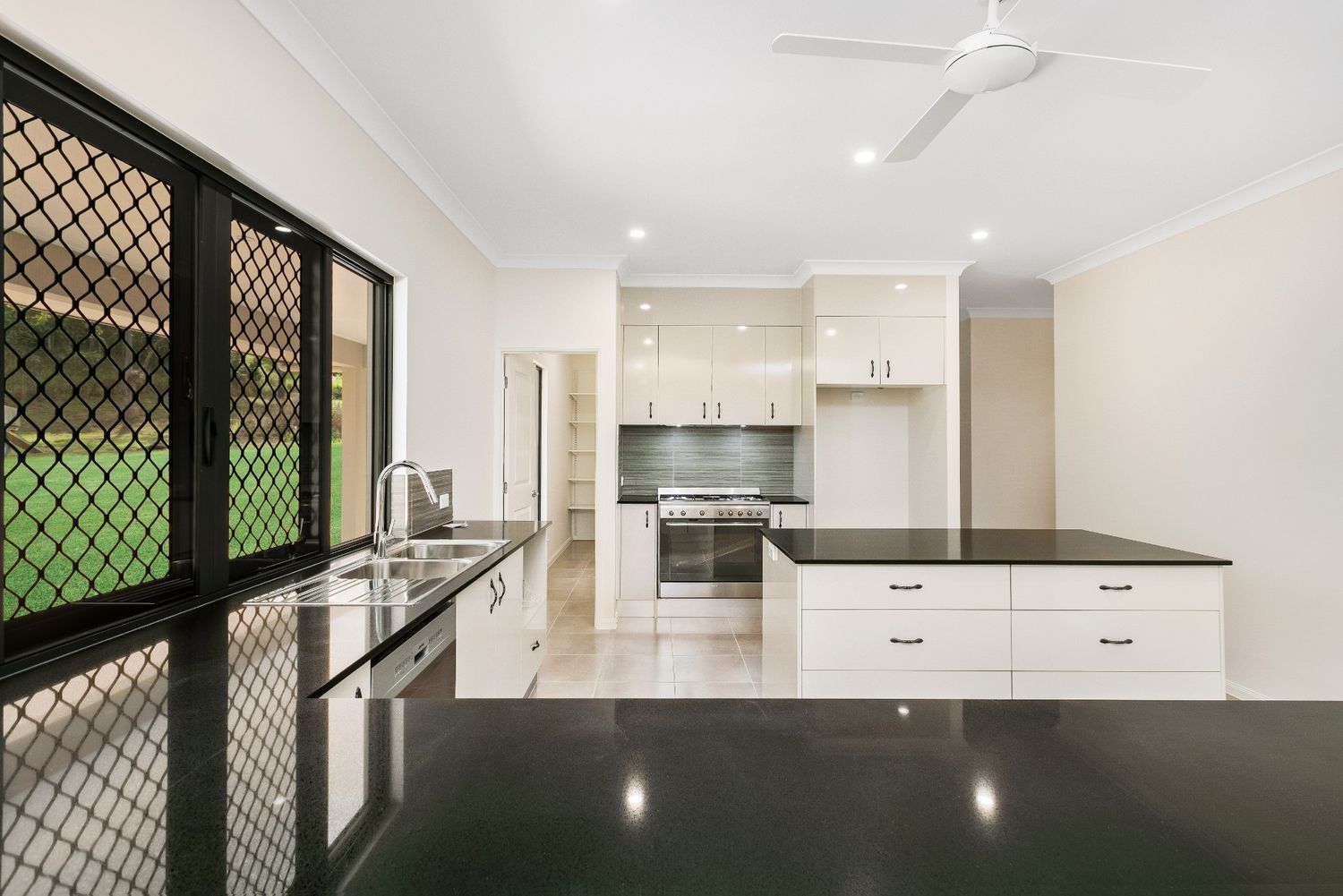 A Kitchen With Black Counter Tops and White Cabinets and a Ceiling Fan — Ashlee Jones Homes in Gordonvale, QLD
