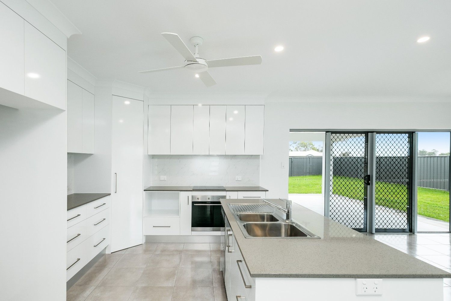 A Kitchen With White Cabinets, Granite Counter Tops, Stainless Steel Appliances and a Ceiling Fan — Ashlee Jones Homes in Gordonvale, QLD