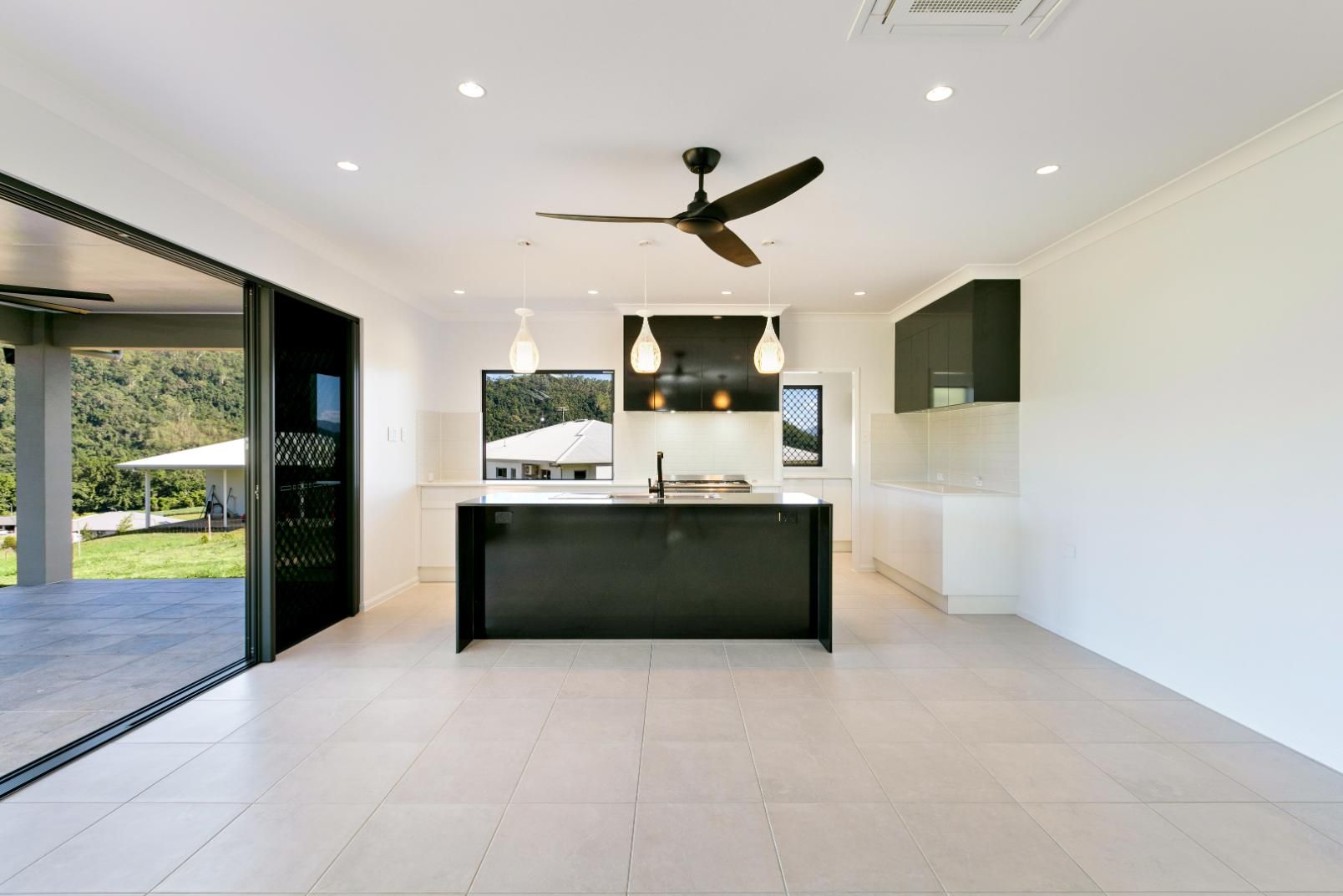 An Empty Kitchen With a Black Island and a Ceiling Fan — Ashlee Jones Homes in Gordonvale, QLD