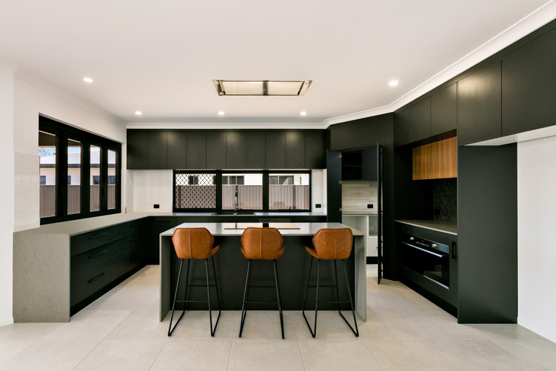 A Kitchen With Black Cabinets and Stools and a Large Island — Ashlee Jones Homes in Gordonvale, QLD