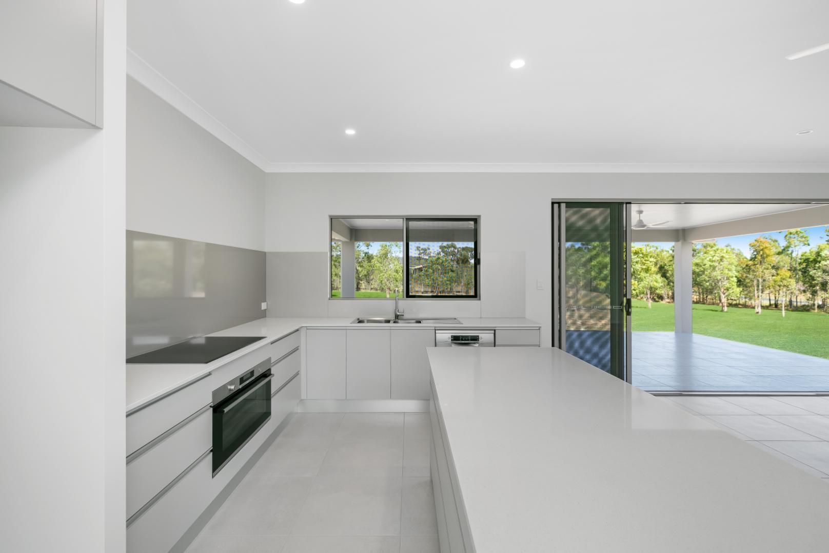 A Kitchen With White Cabinets and a Sliding Glass Door — Ashlee Jones Homes in Gordonvale, QLD