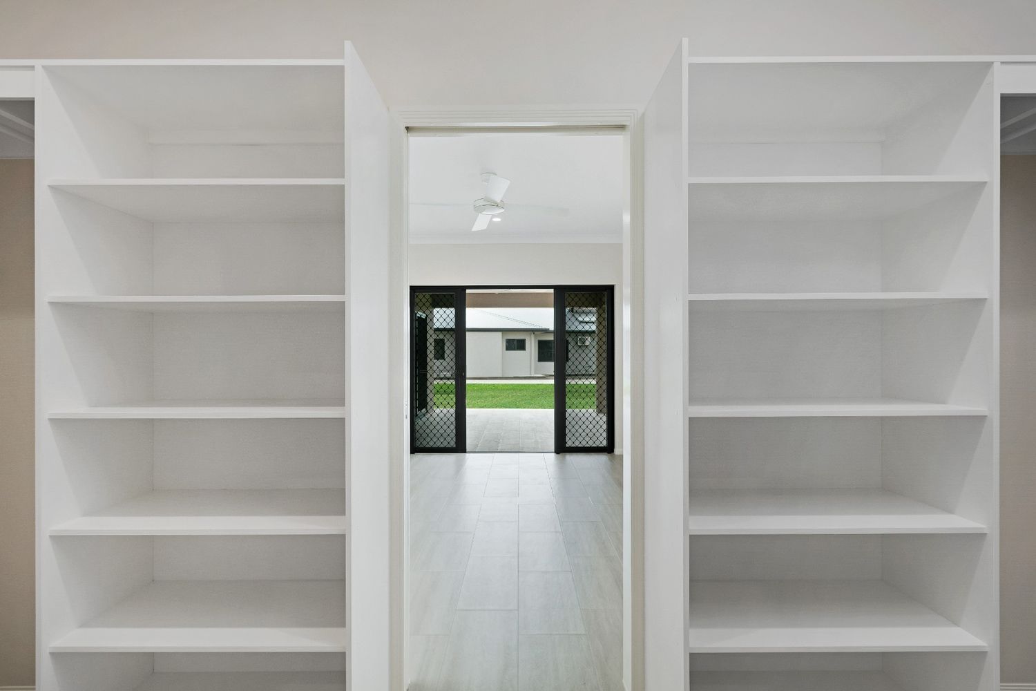 A Walk in Closet With Lots of Shelves and a Door Leading to a Living Room — Ashlee Jones Homes in Gordonvale, QLD