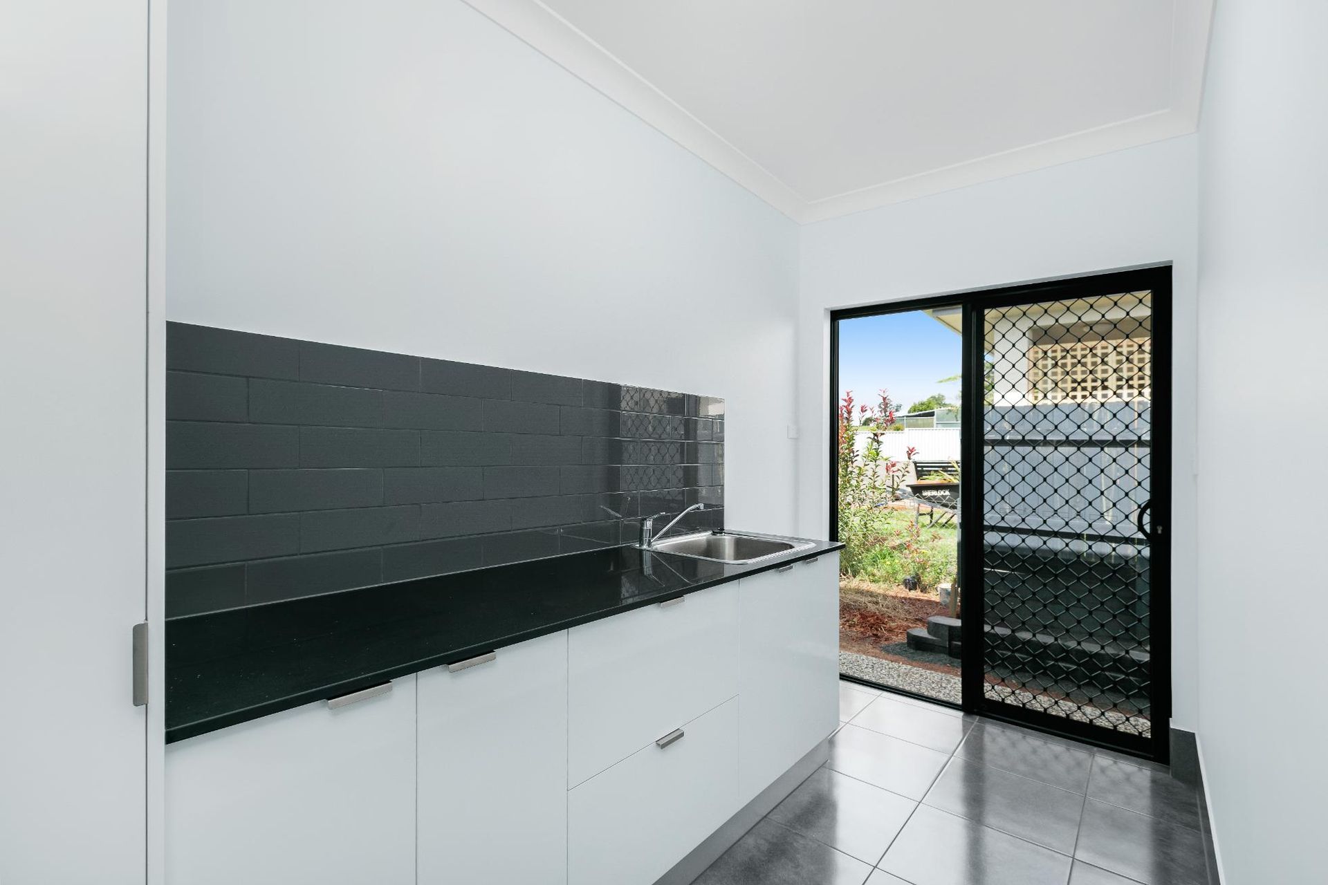 A Kitchen With White Cabinets and Black Counter Tops and a Sliding Glass Door — Ashlee Jones Homes in Gordonvale, QLD