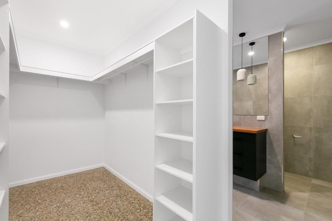 A Walk in Closet With White Shelves and a Bathroom in the Background — Ashlee Jones Homes in Gordonvale, QLD