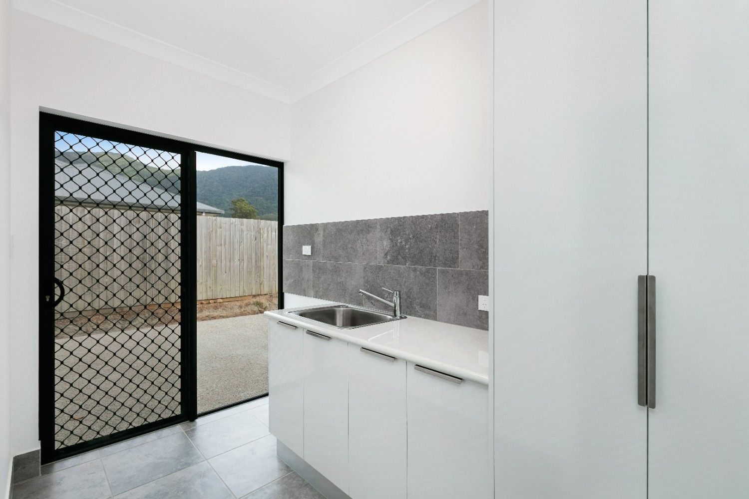 A Kitchen With a Sink and a Sliding Glass Door Leading to a Backyard — Ashlee Jones Homes in Gordonvale, QLD