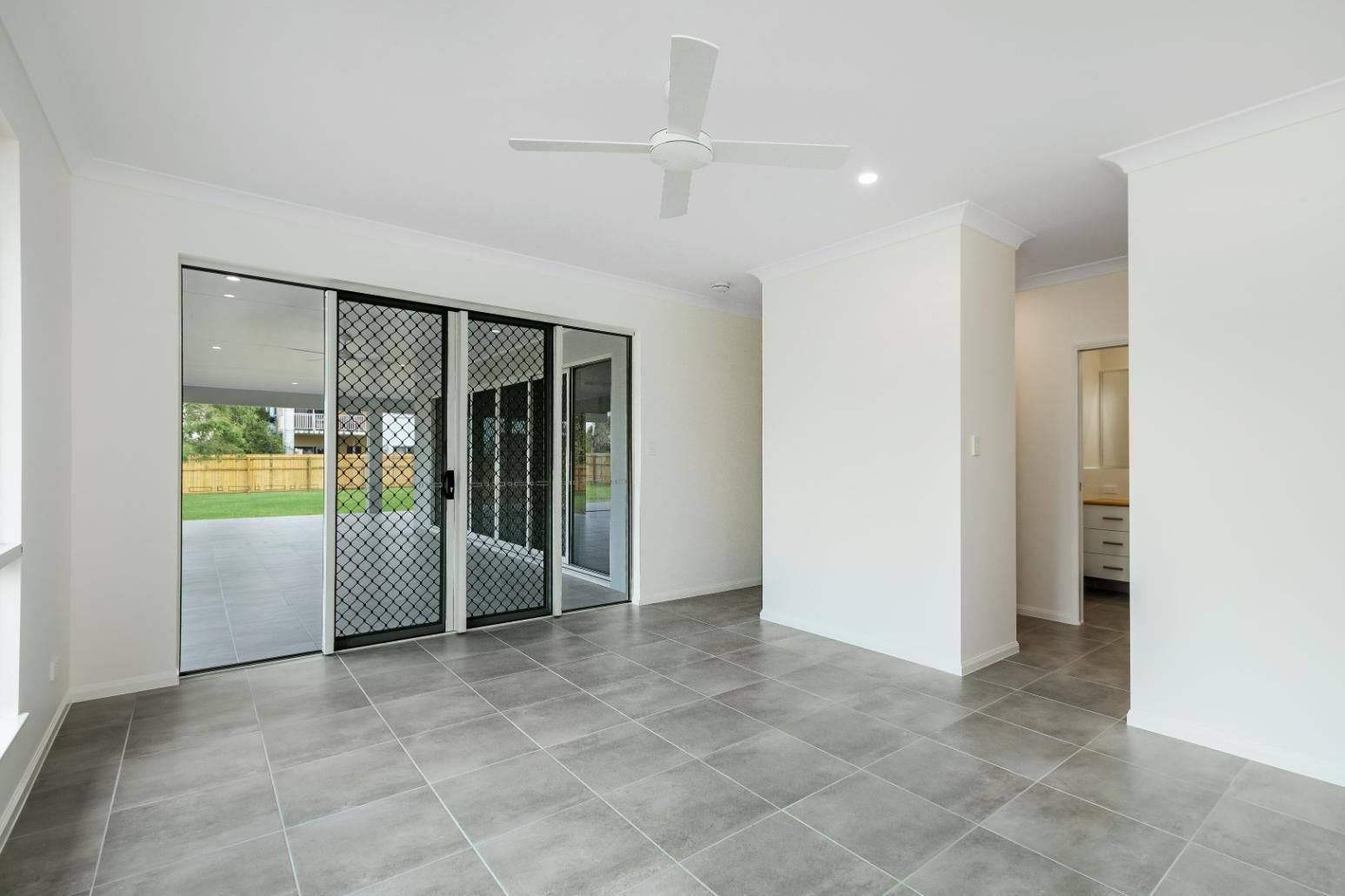 An Empty Living Room With a Ceiling Fan and Sliding Glass Doors — Ashlee Jones Homes in Gordonvale, QLD