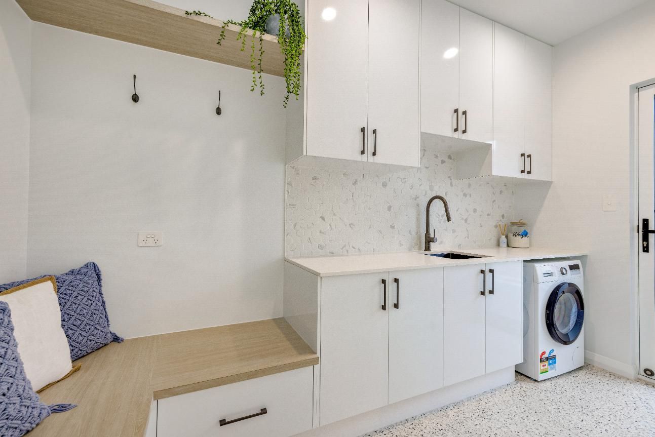 A Laundry Room With White Cabinets, a Washer and Dryer, and a Bench — Ashlee Jones Homes in Gordonvale, QLD