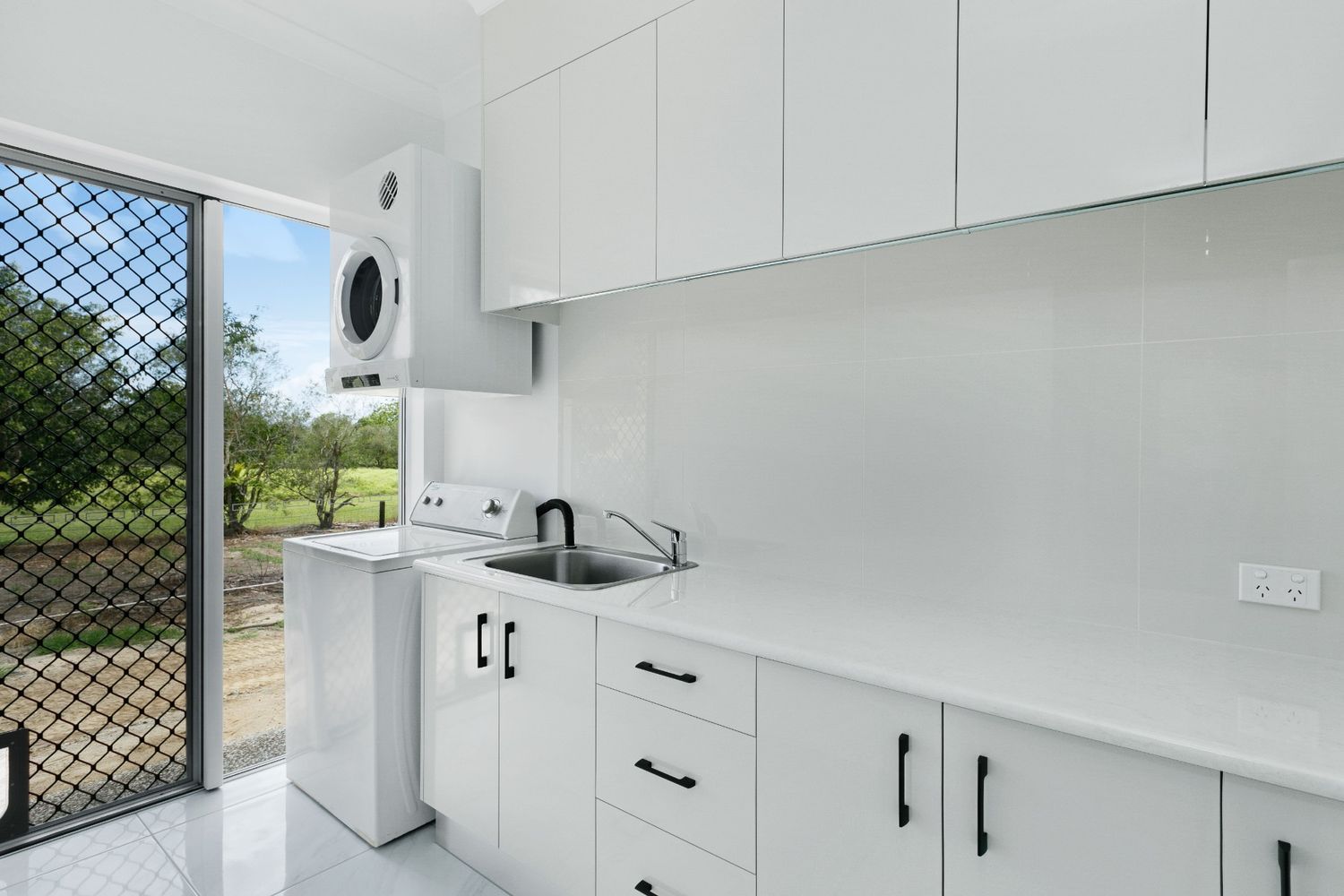 A Laundry Room With White Cabinets, a Sink, and a Washer and Dryer — Ashlee Jones Homes in Gordonvale, QLD
